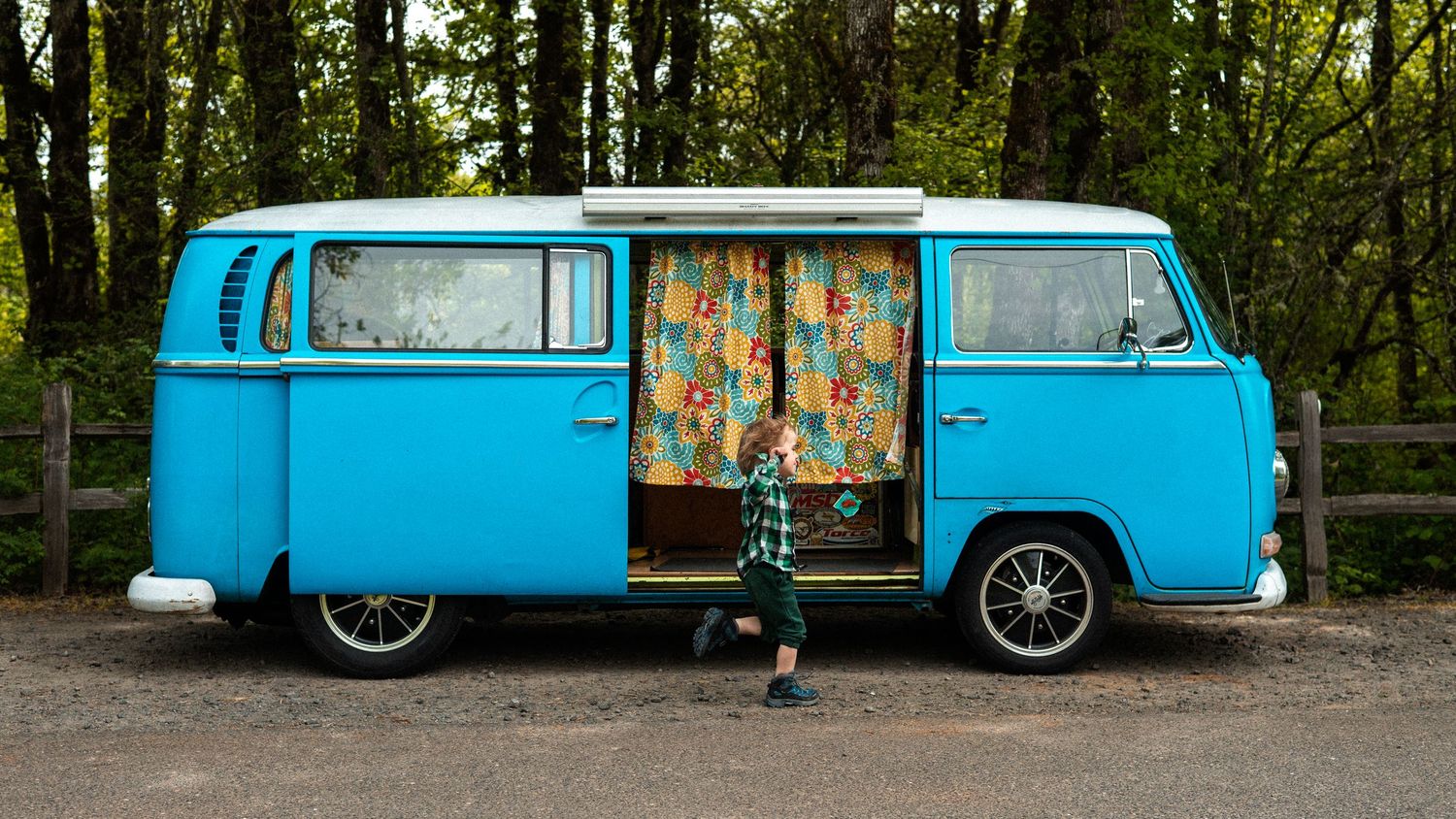 A bright turquoise vintage VW bus parked on a forest road.