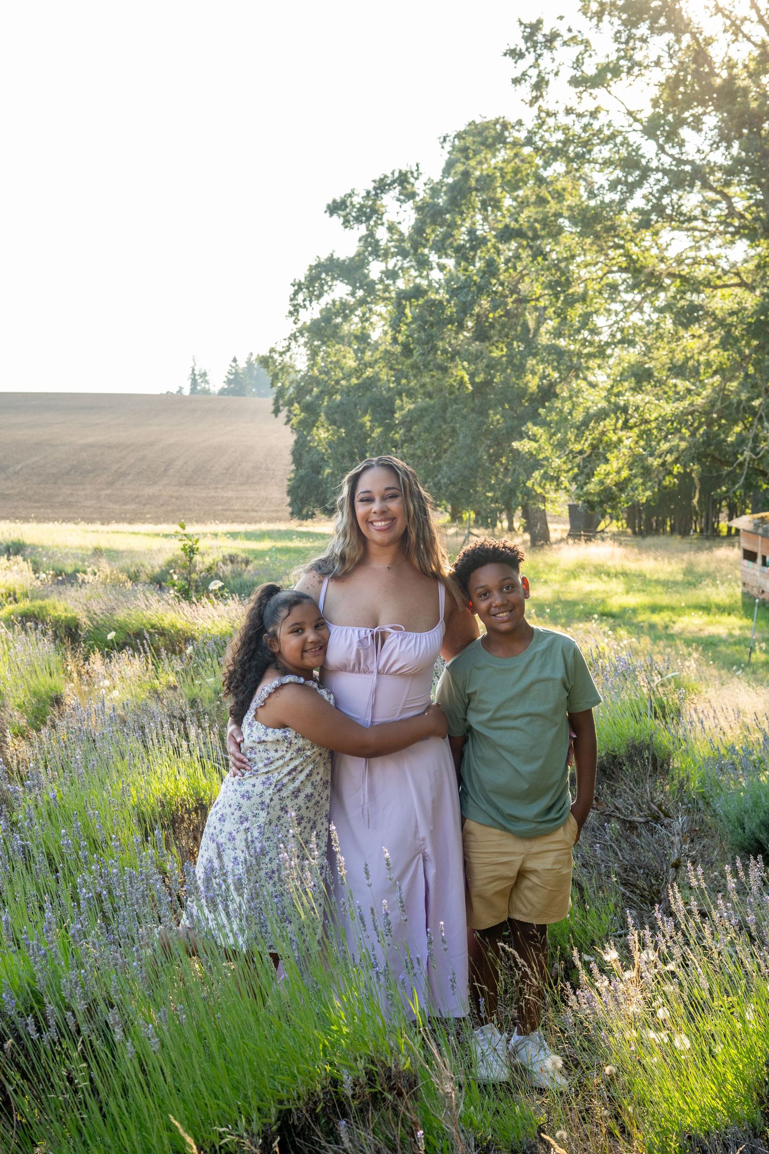 Three people stand together smiling in a lavender field on a sunny summer day.
