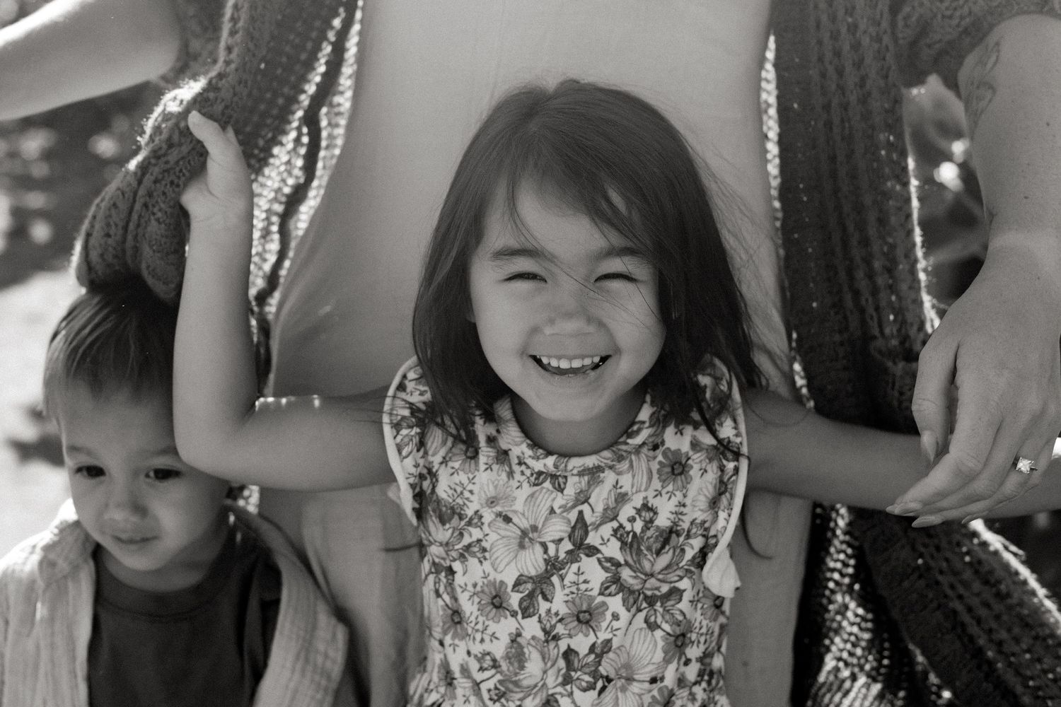 A joyful child in a floral dress smiles brightly while playing on playground equipment in black and white.