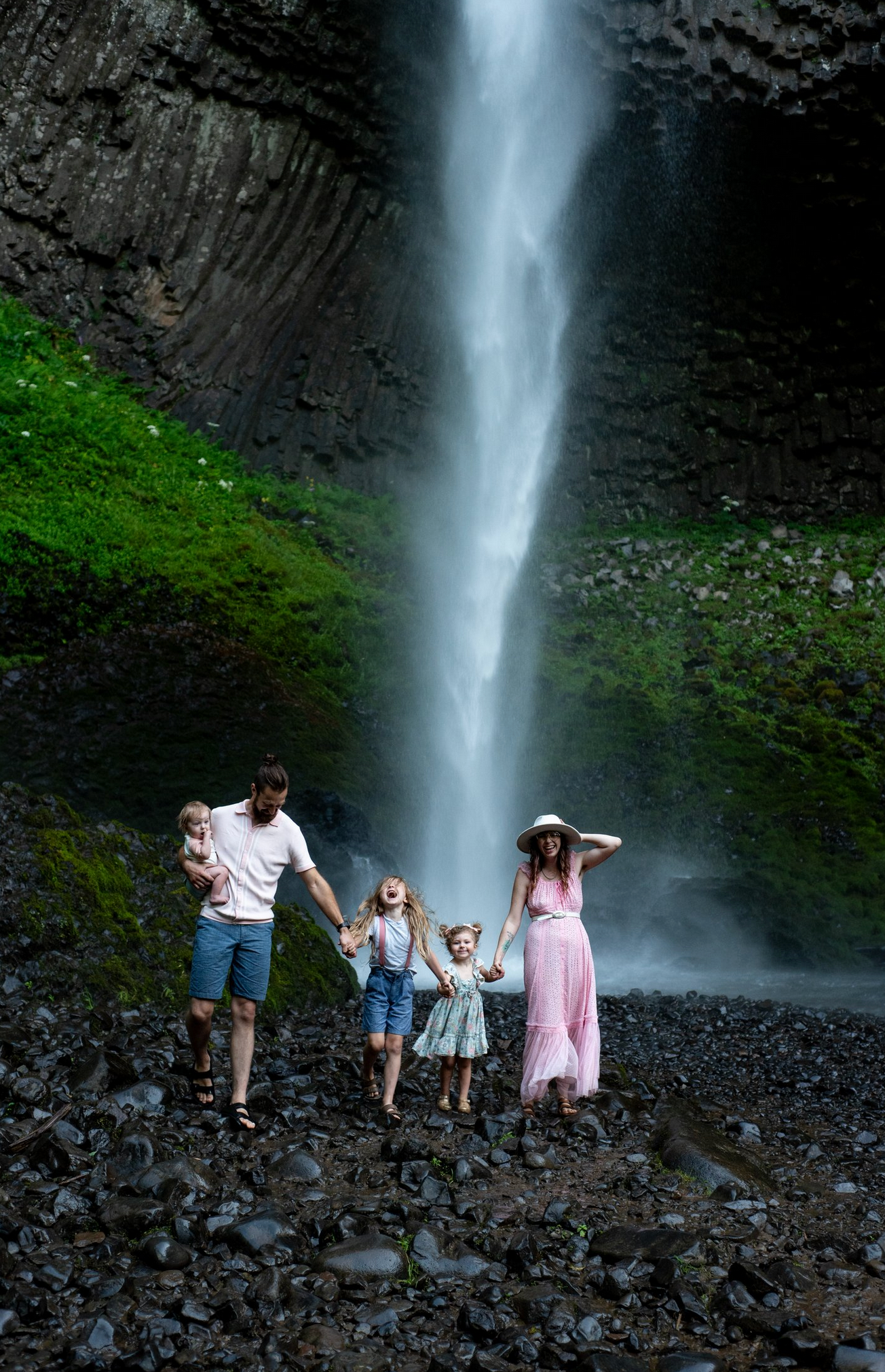 A stunning waterfall cascades behind a family enjoying a nature hike along a rocky trail.
