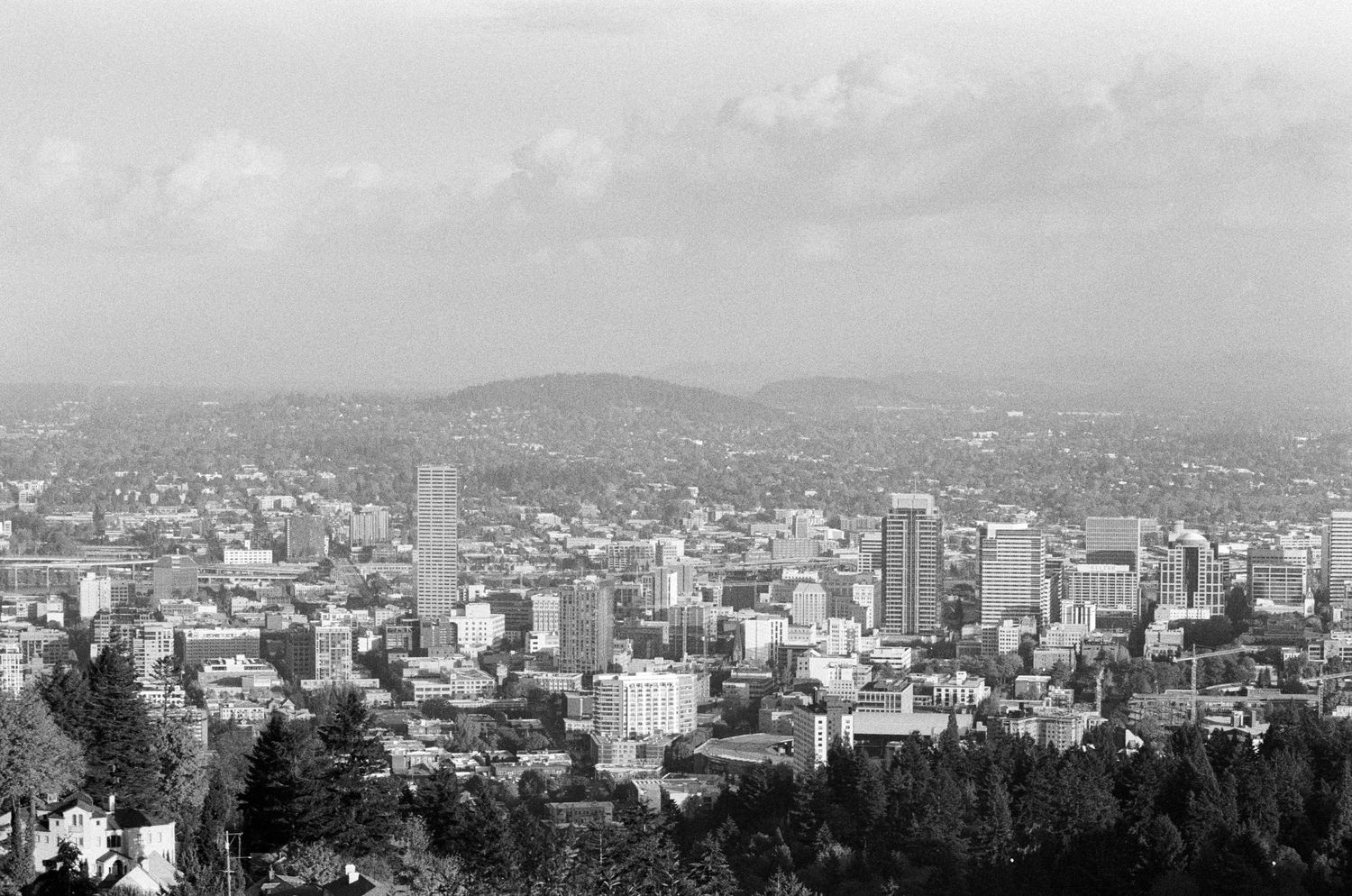 Black and white panoramic cityscape view of Portland Oregon with mountains and buildings visible in the distance.
