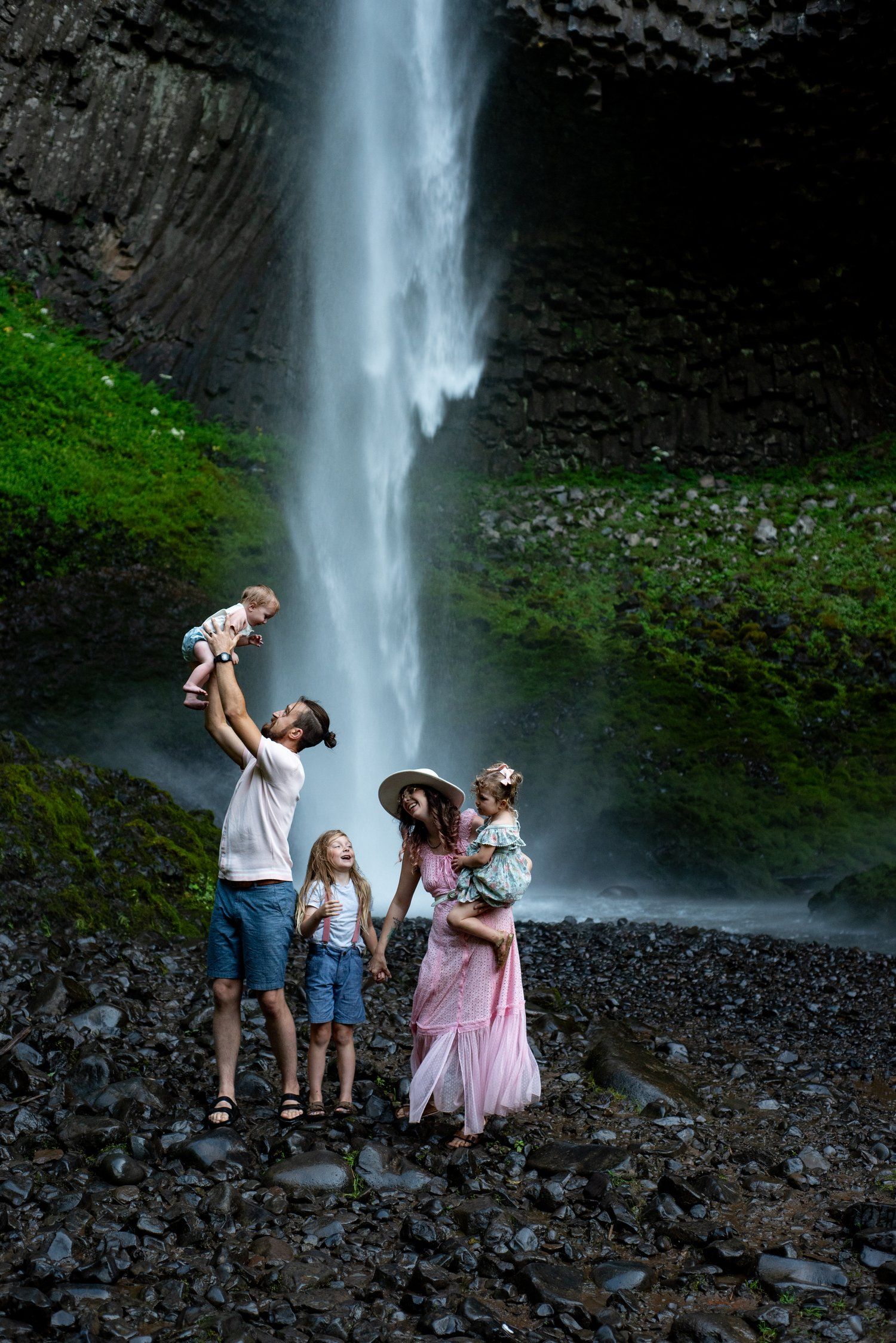 A family enjoys a majestic waterfall view together on rocky terrain.