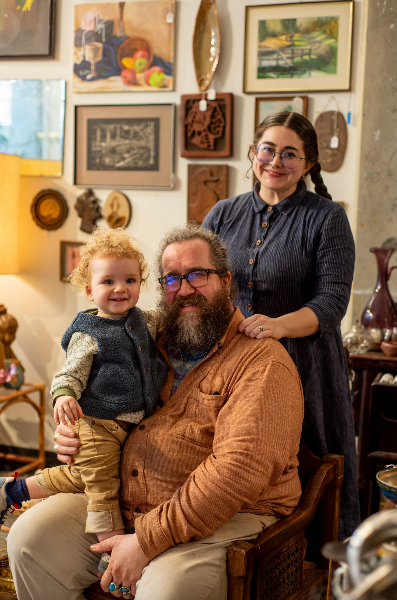 Family portrait in a cozy room decorated with vintage artwork and collectibles on the walls.