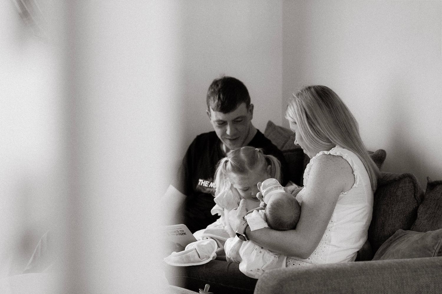 A black and white photo of parents sitting on a sofa lovingly holding their two young children.