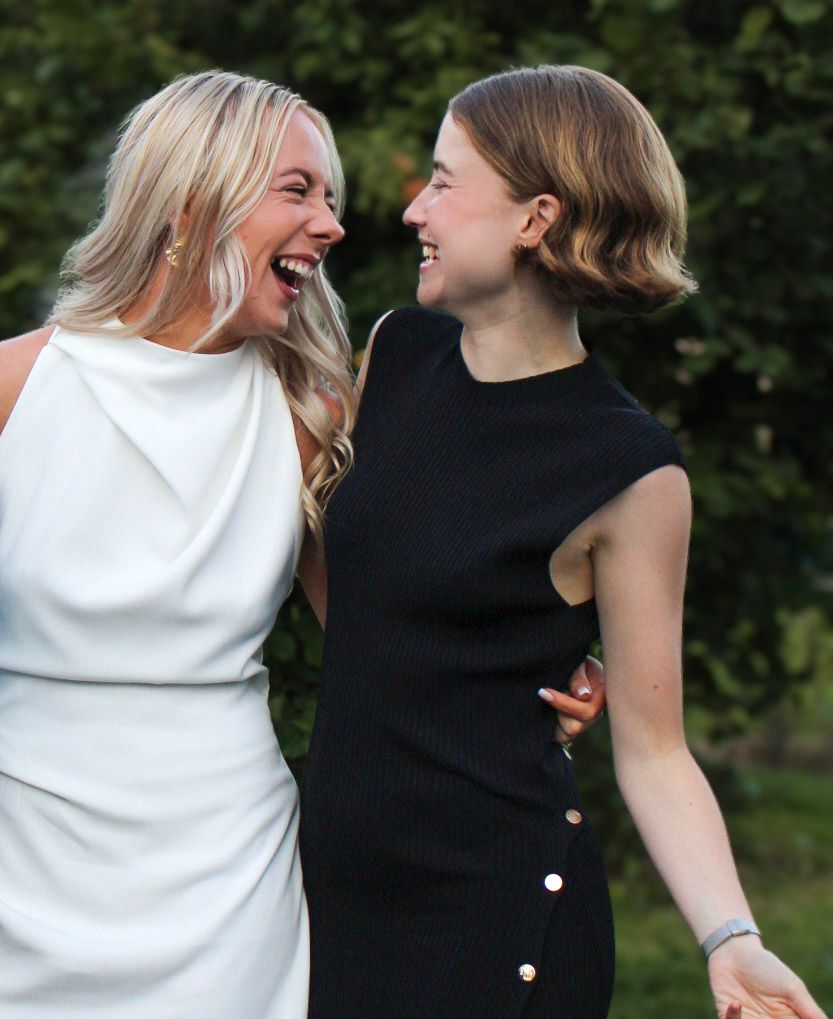 Two women in white and black dresses laughing joyfully outdoors.