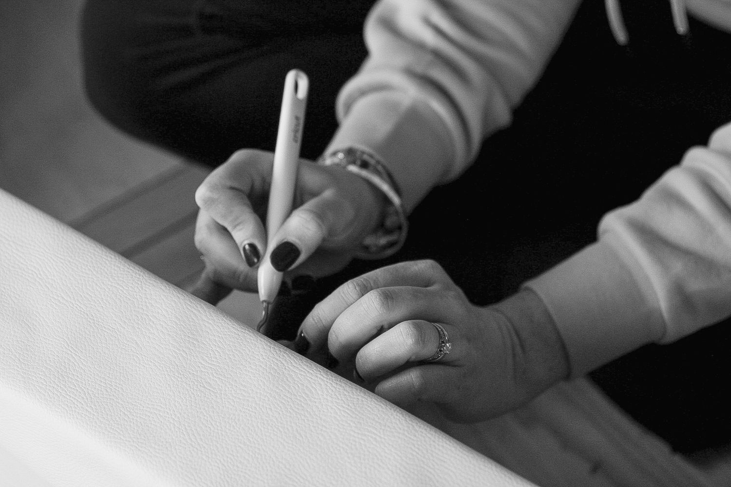 Close-up black and white photo of hands writing with a marker pen on a surface.