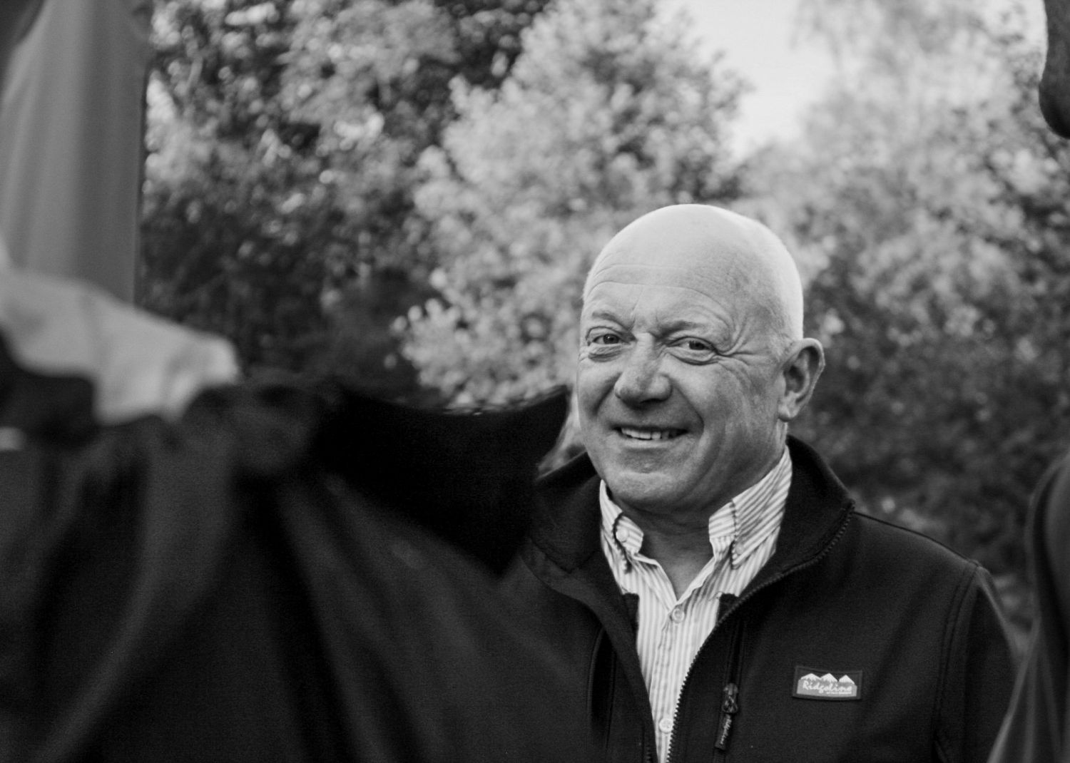 Smiling bald elderly man laughing outdoors in black and white photo.