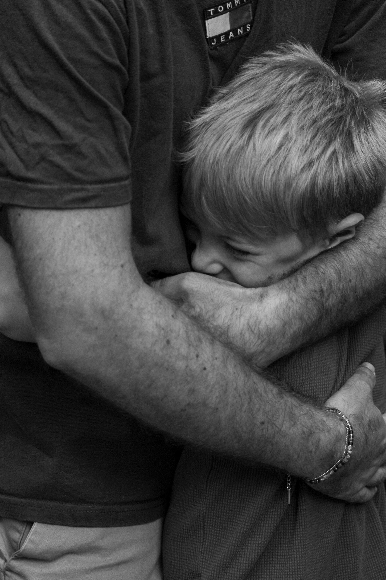 A young boy hugs an adult tightly in an emotional black and white close-up photograph.