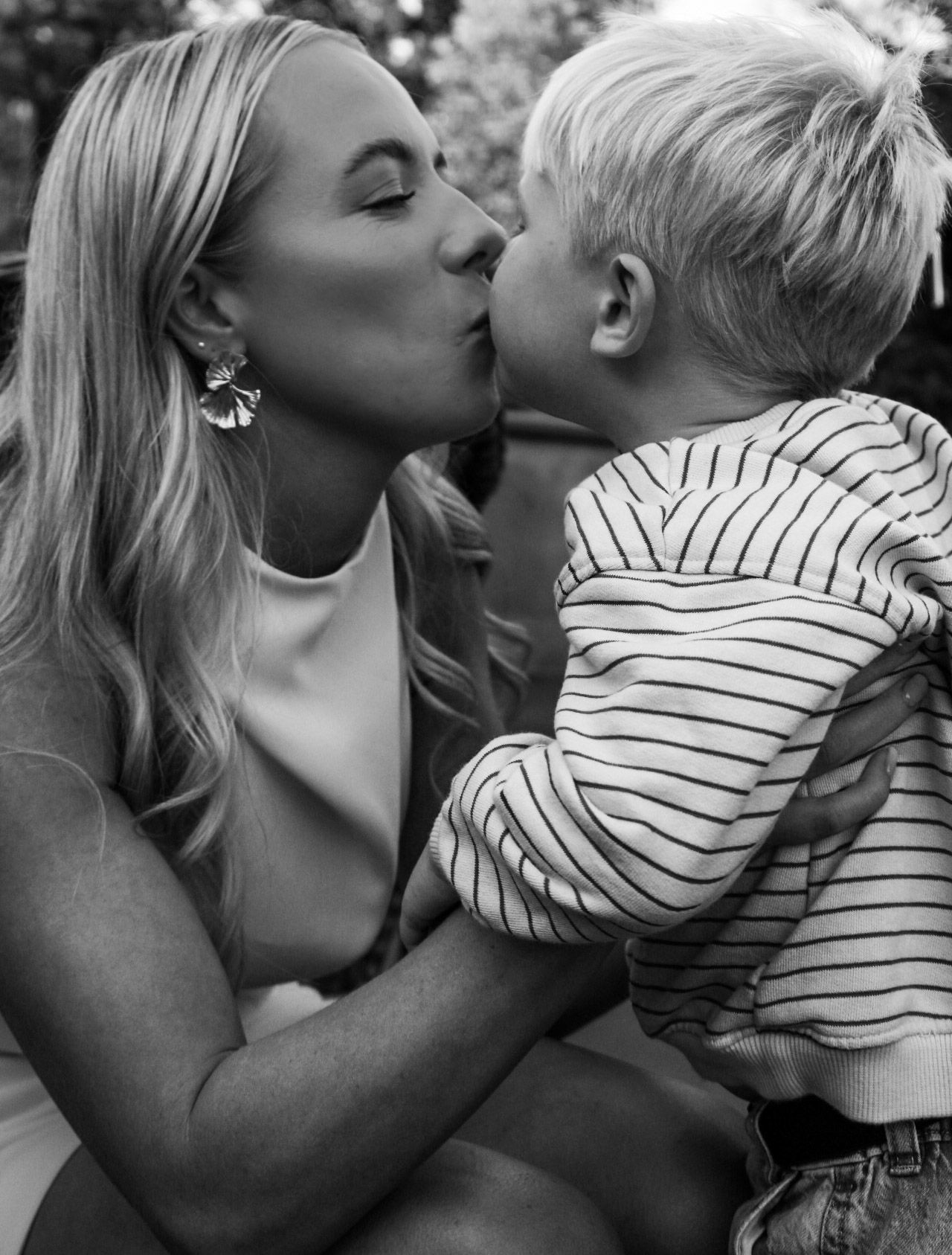 Mother kissing young blond son tenderly in black and white portrait.