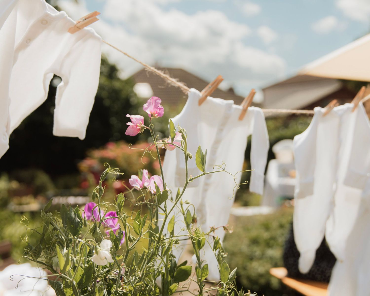 White baby clothes hang on a clothesline with pink flowers at an outdoor baby shower celebration.