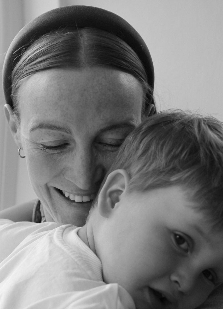 Black and white photo of a smiling mother with a headband cuddling her young toddler child.