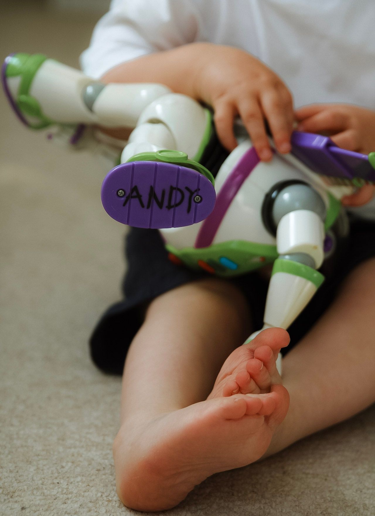 A child sits on the floor playing with a Buzz Lightyear toy marked with the name Andy.