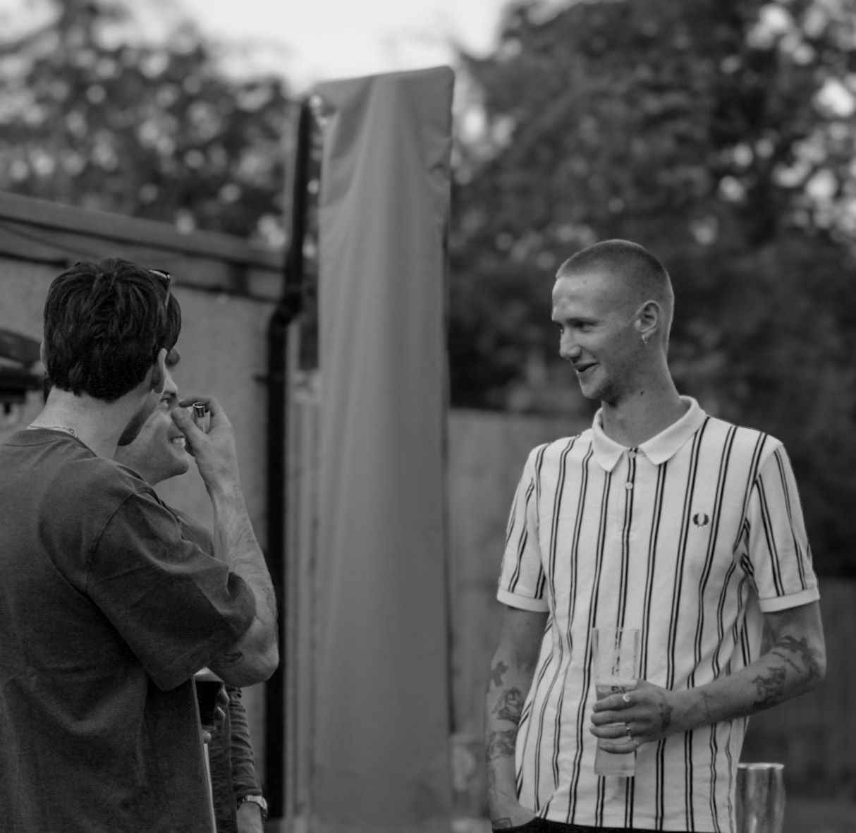 Two young men chat and laugh outdoors at an event, captured in black and white photography.