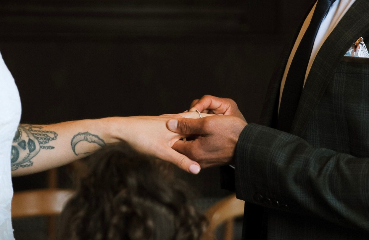 Groom placing wedding ring on brides tattooed hand during ceremony.
