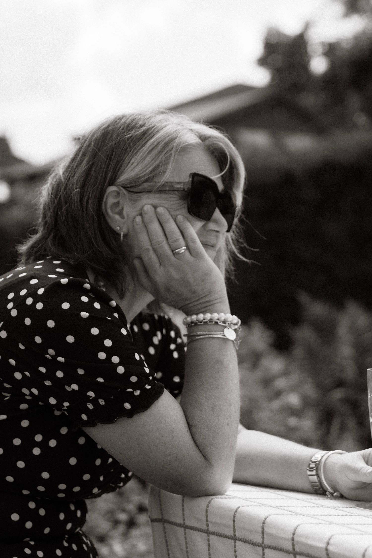 Black and white portrait of a blonde woman in sunglasses and polka dot dress resting her hand on her face.