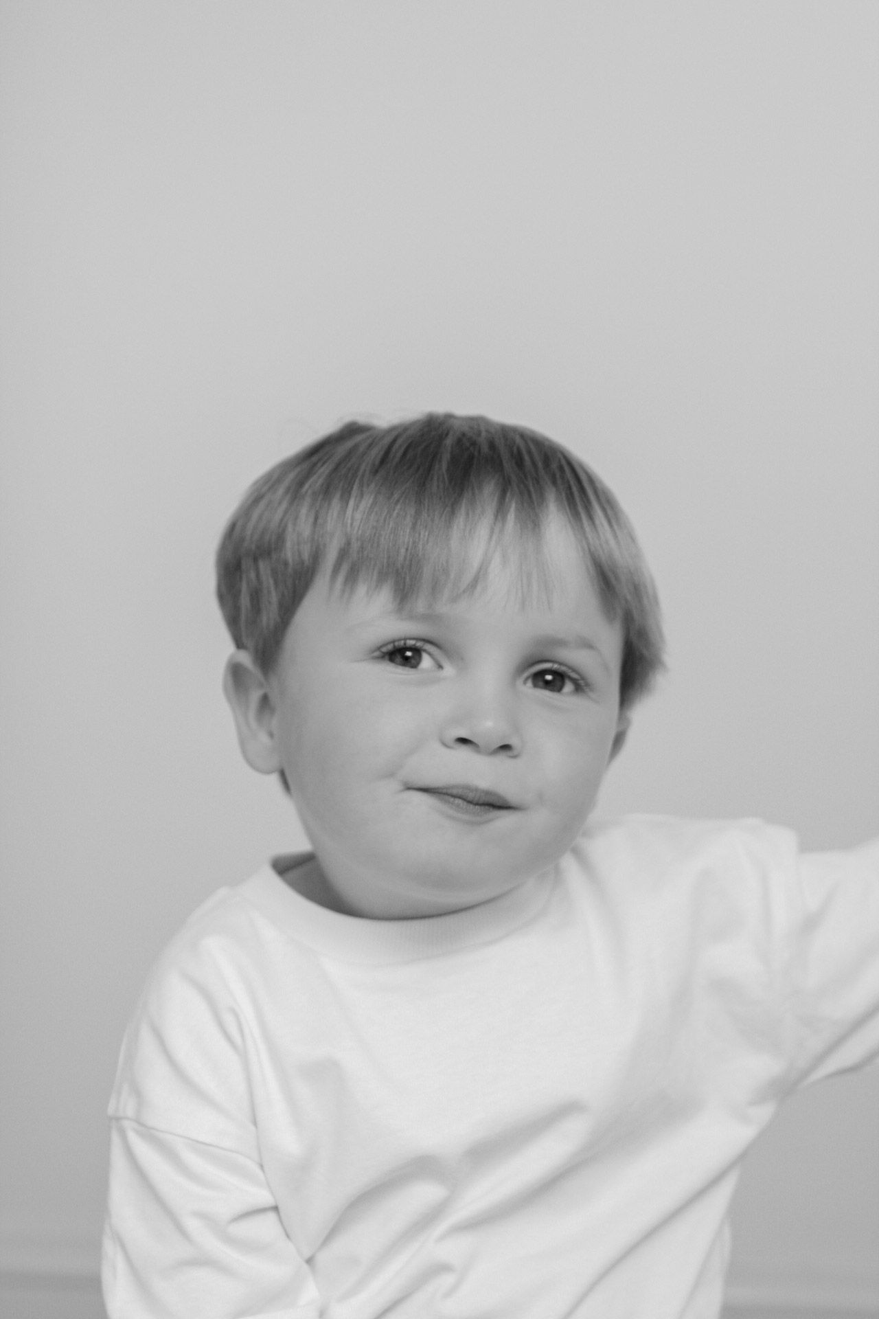 Black and white portrait of a smiling toddler in a white long-sleeve shirt against a light background.