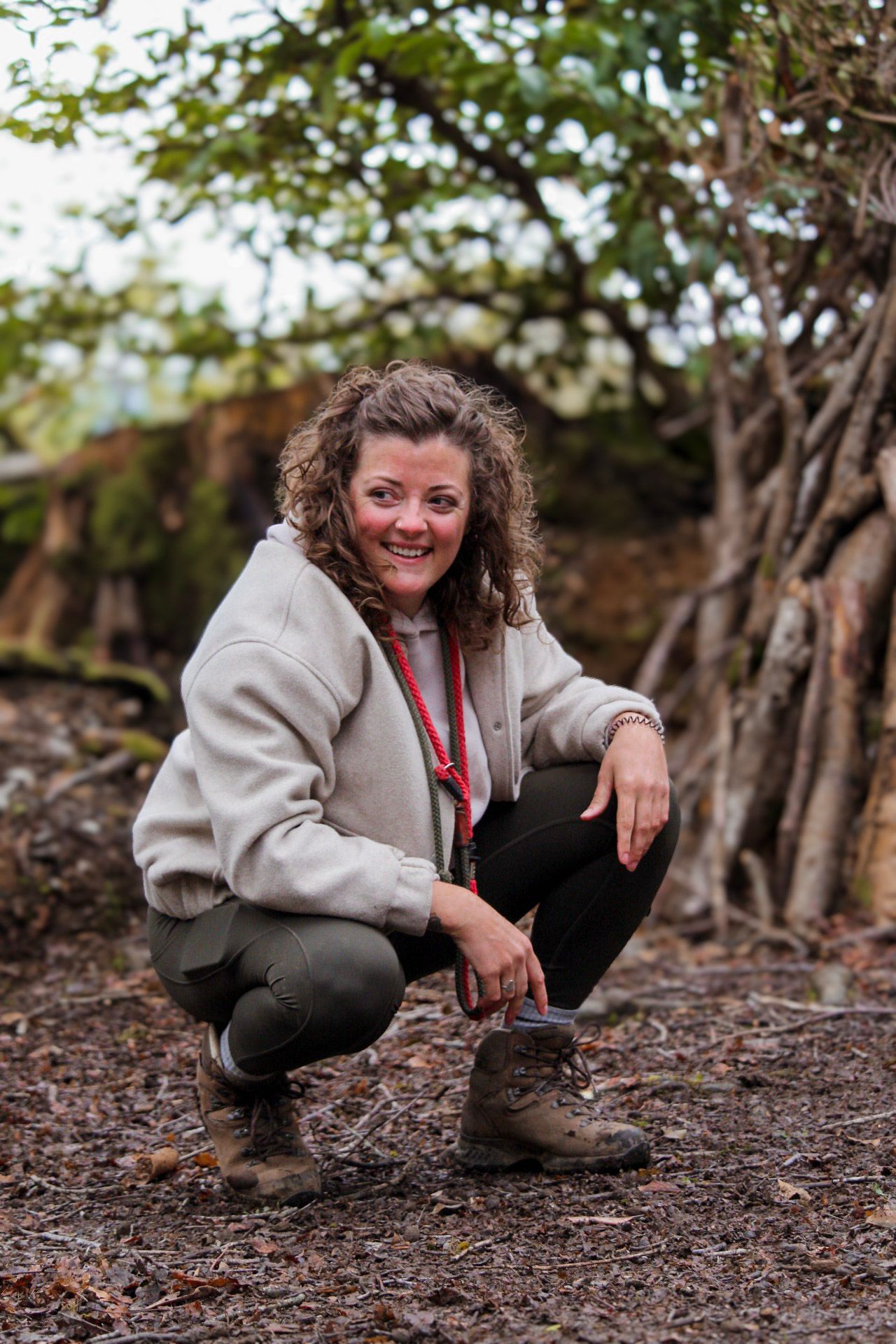 Smiling woman crouching in hiking boots and fleece jacket in a woodland setting.