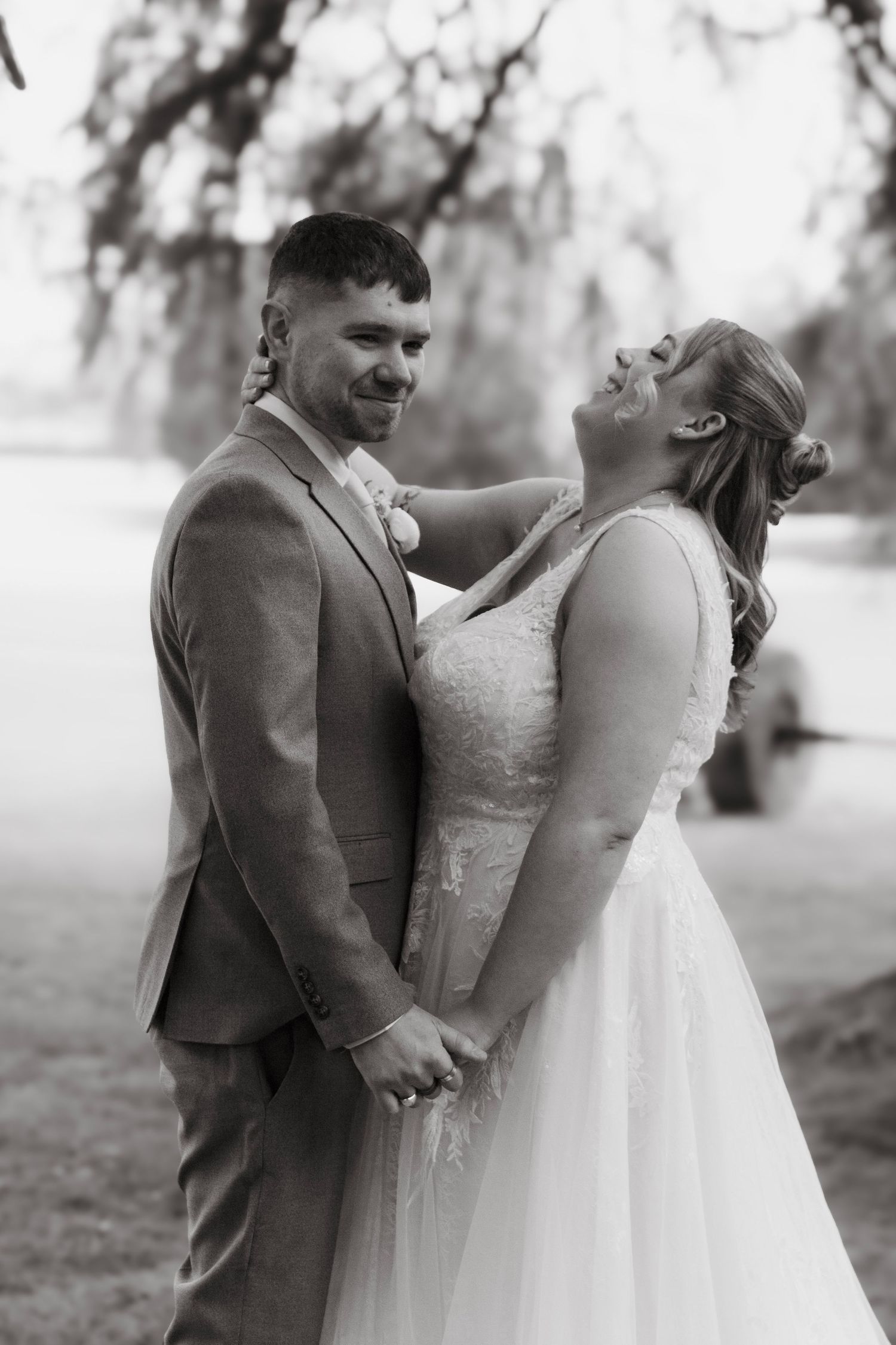 Black and white photo of a bride and groom holding hands and smiling outdoors on their wedding day.