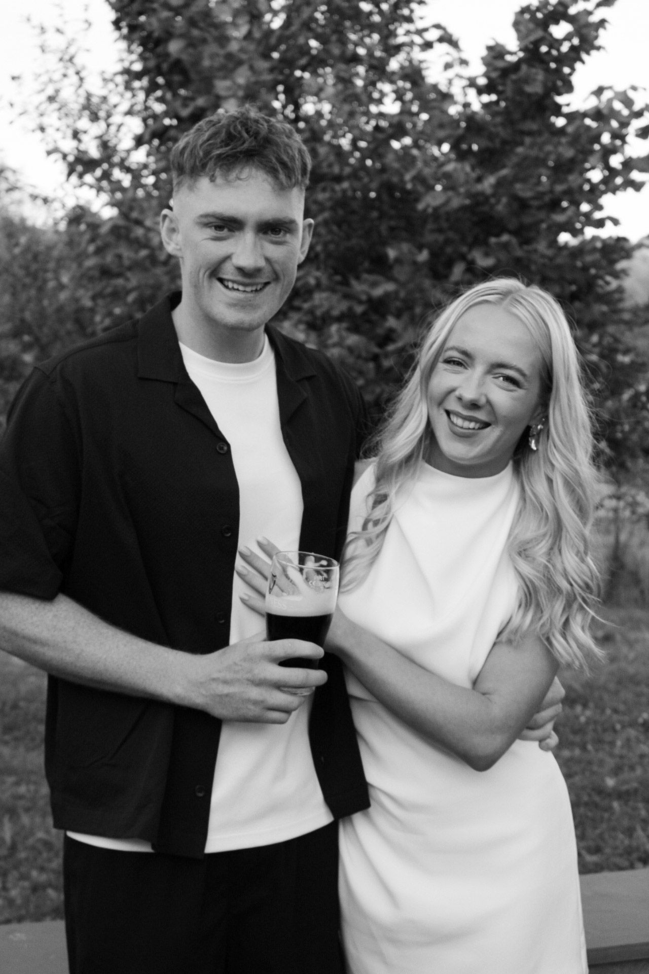 Happy couple smiling together holding a dark beer in black and white photo.