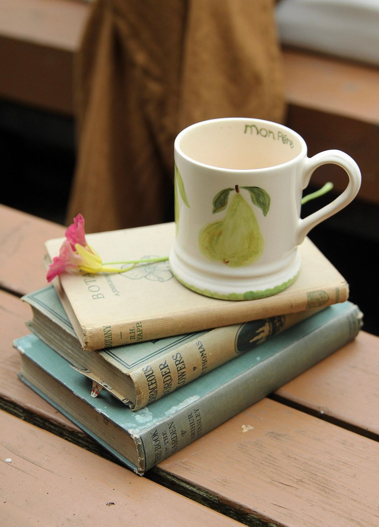 A ceramic mug with pear design sitting atop a stack of vintage books with a pink flower beside it.