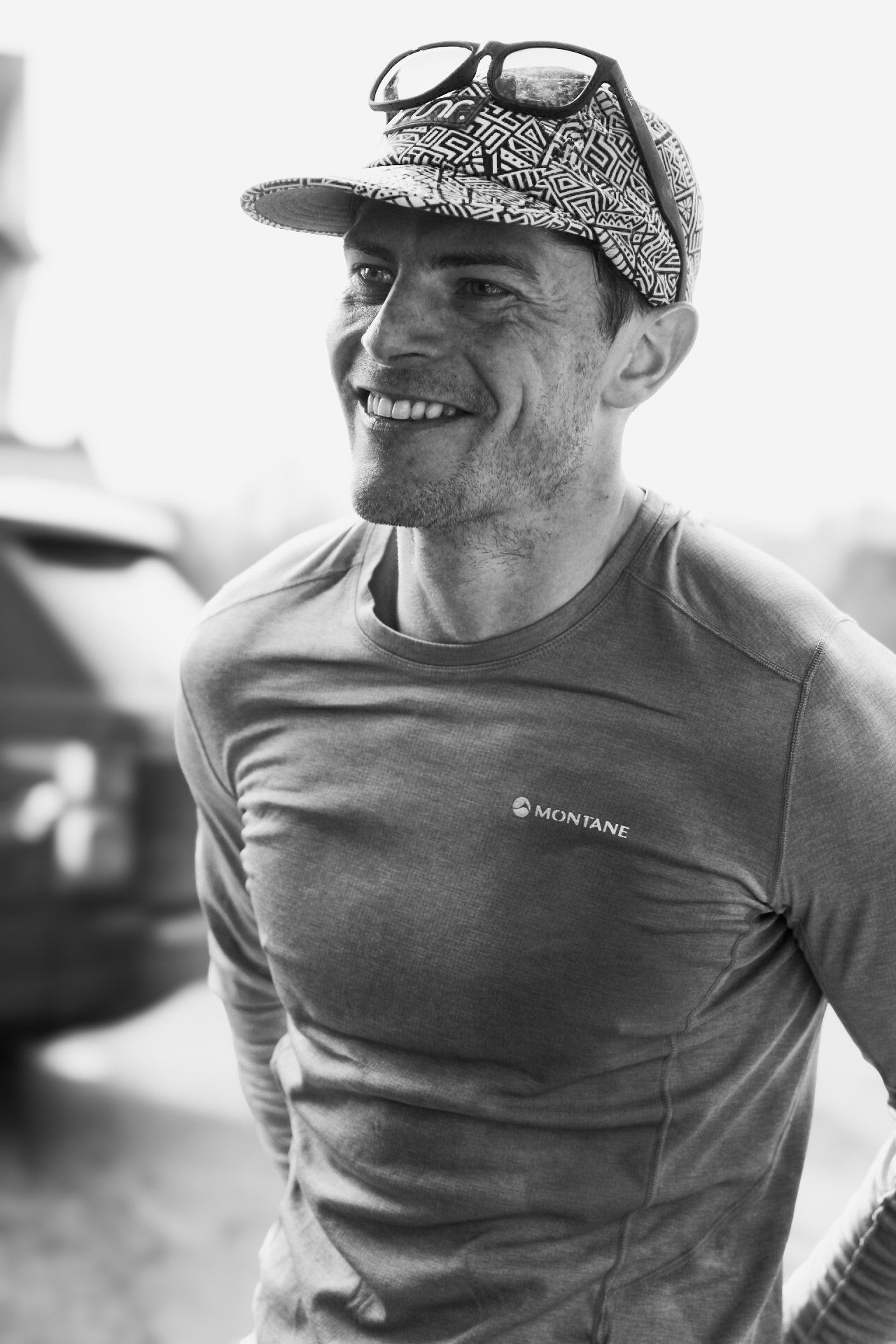 Smiling athletic man wearing a Montane shirt and patterned cap, black and white photo.