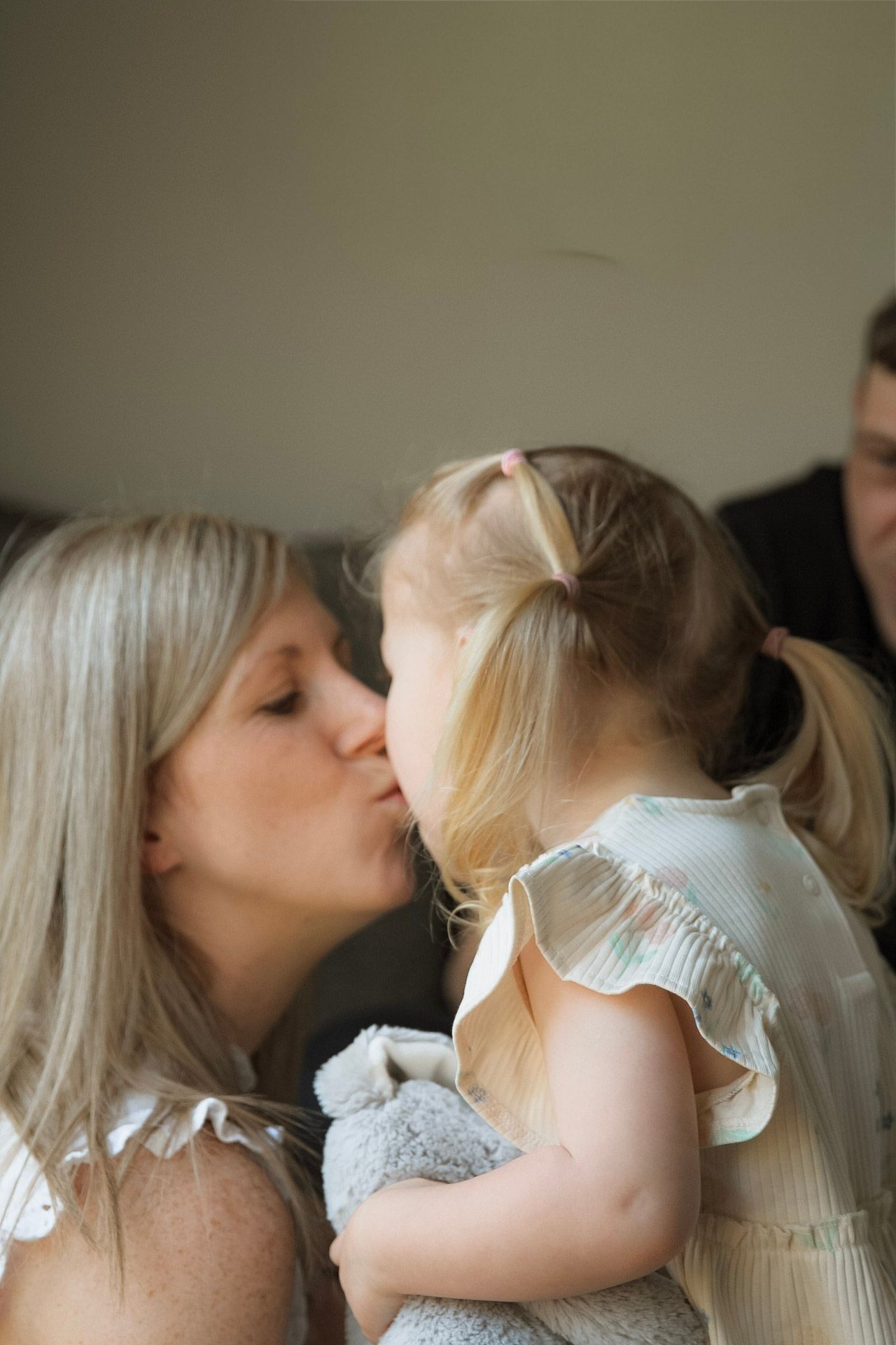 A mother kissing her young blonde daughter on the lips indoors.