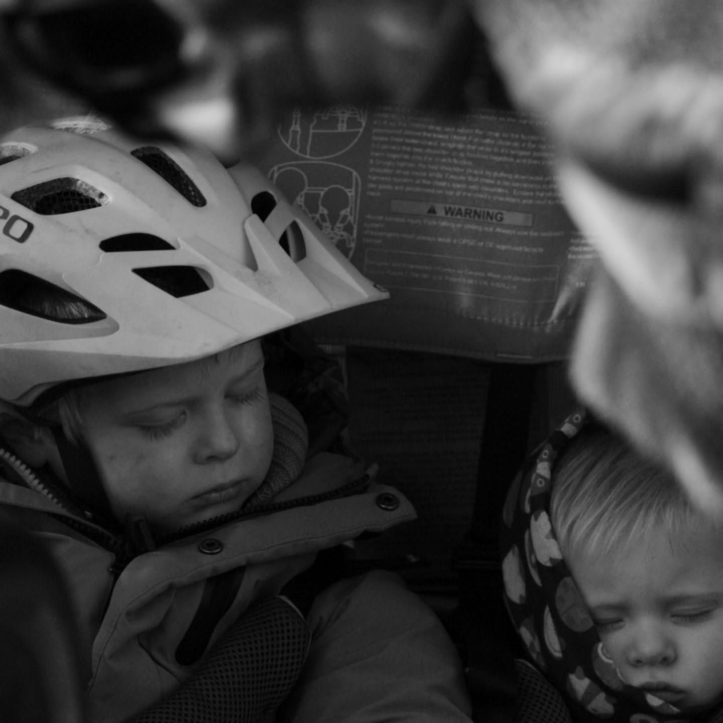 Child sleeping in bike seat wearing white helmet, black and white photo.
