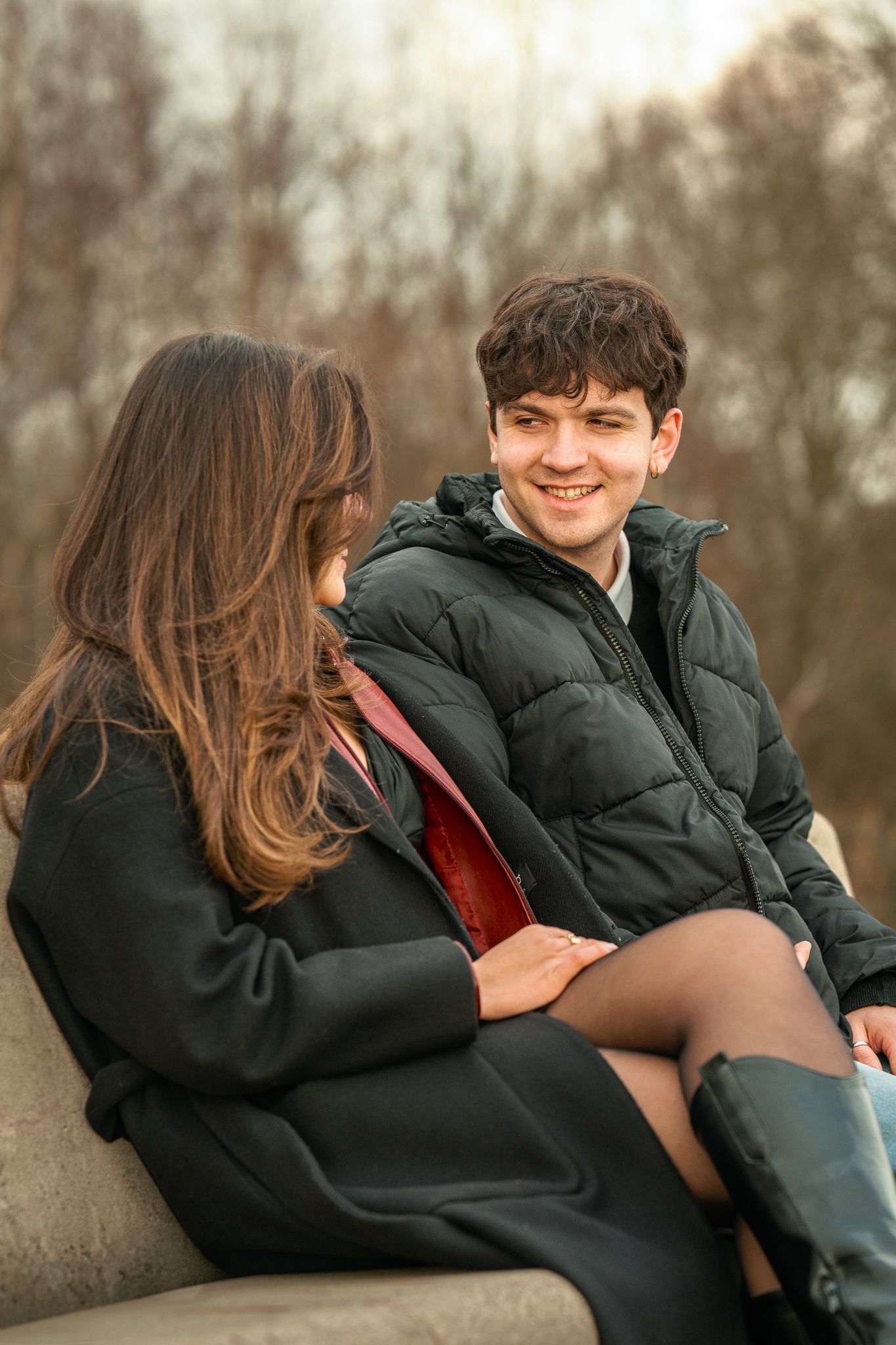 Smiling teenage couple sitting together outdoors in winter coats on stone bench.
