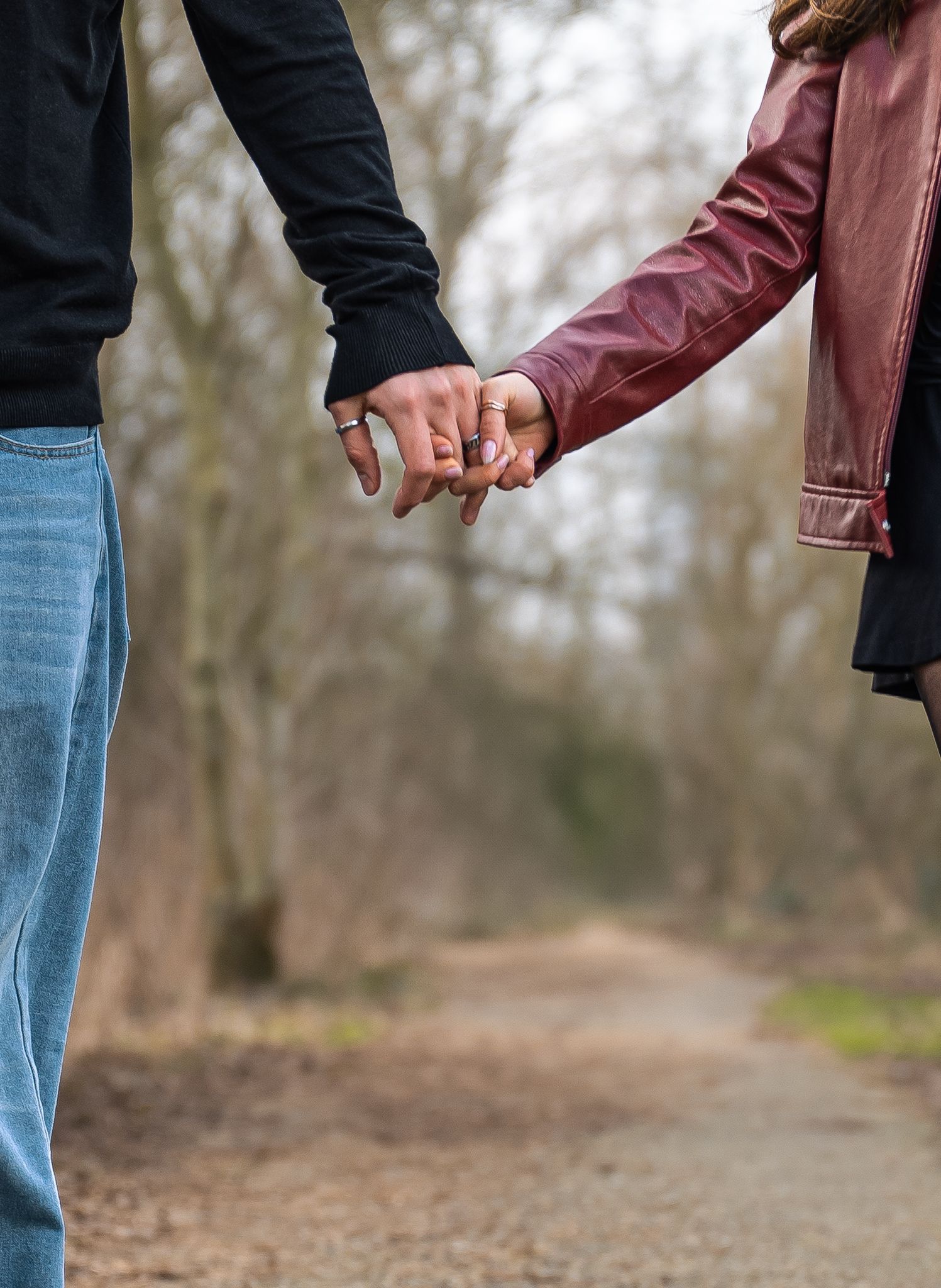 Couple holding hands on a scenic park path surrounded by bare trees in autumn.