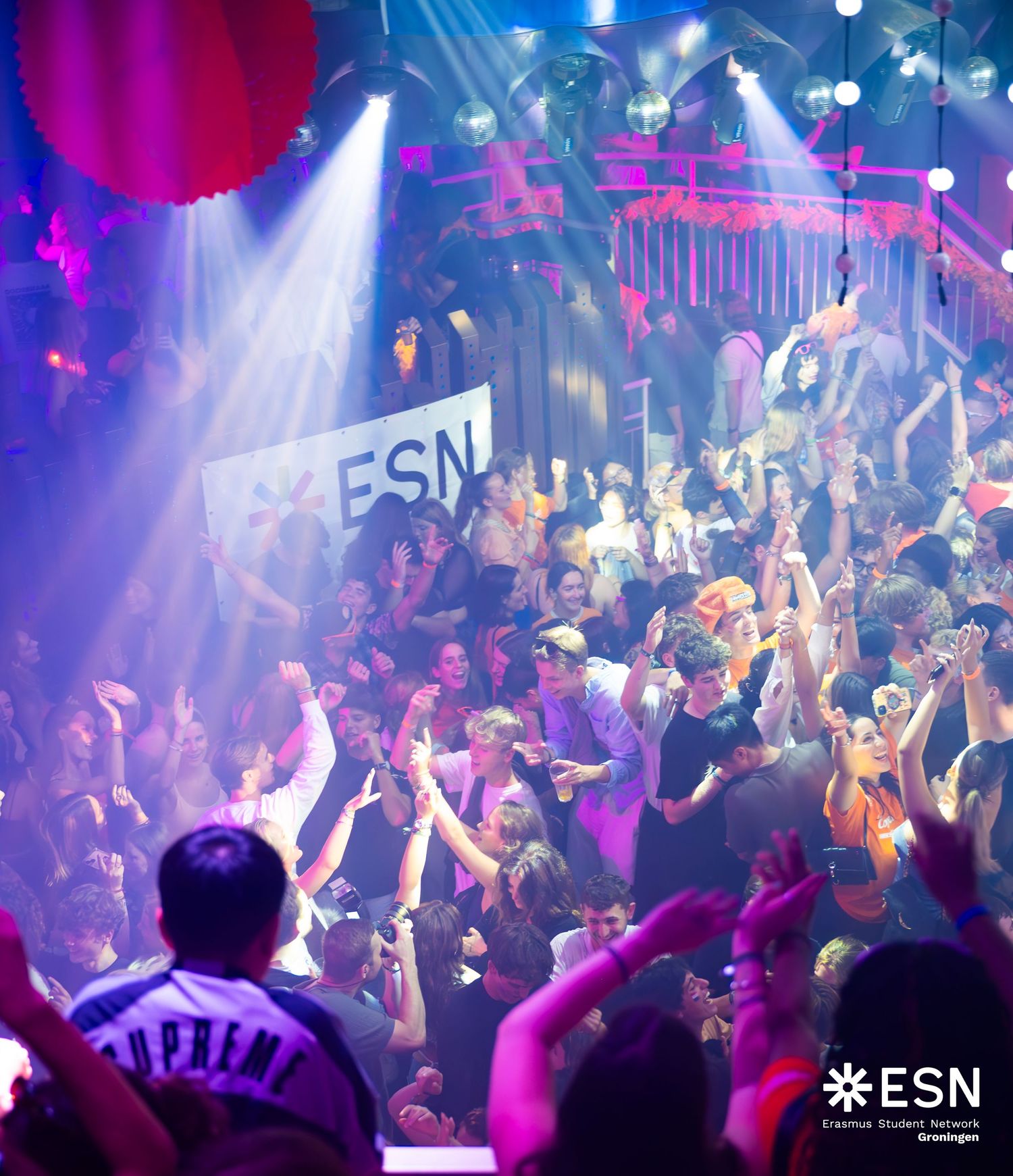 Packed ESN nightclub party with colorful stage lights and crowd cheering with hands raised.