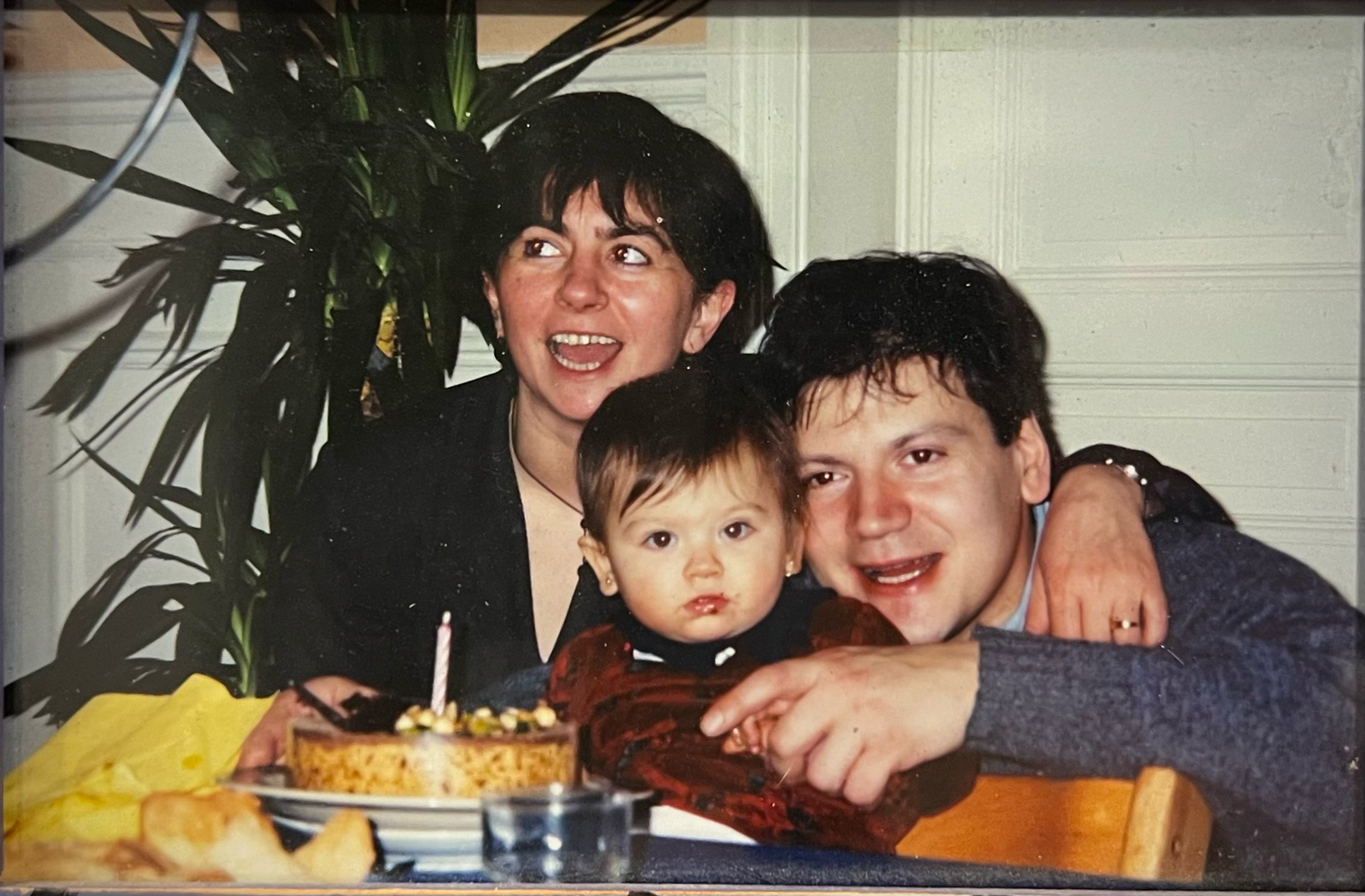 A joyful family of two adults and a baby celebrate a birthday together at a table.