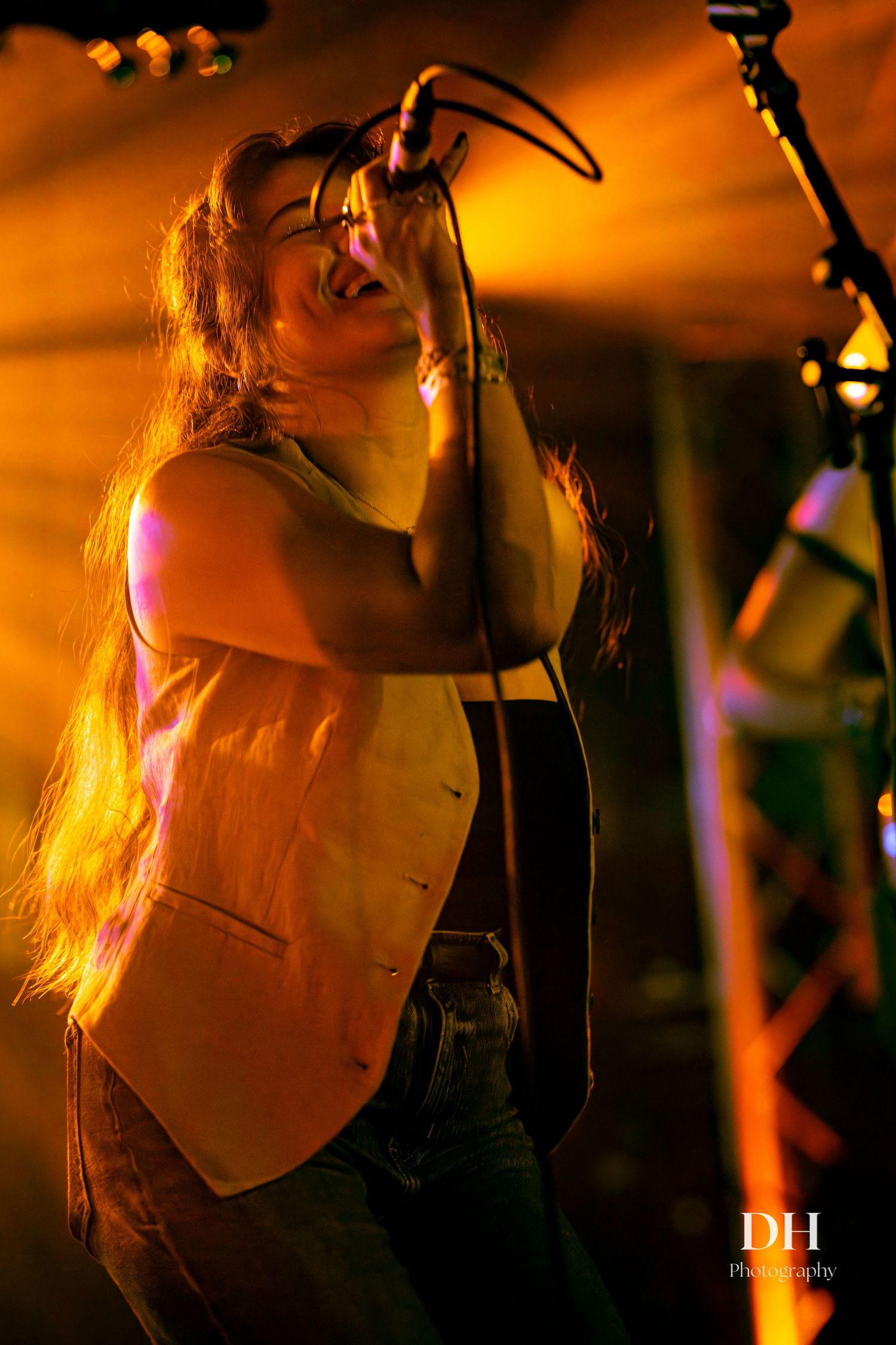 Female vocalist performing passionately on stage under warm golden spotlight at live music event.