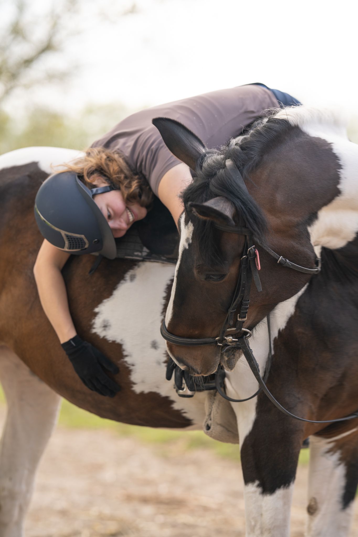 A rider in equestrian gear leans forward affectionately onto a black and white horse.