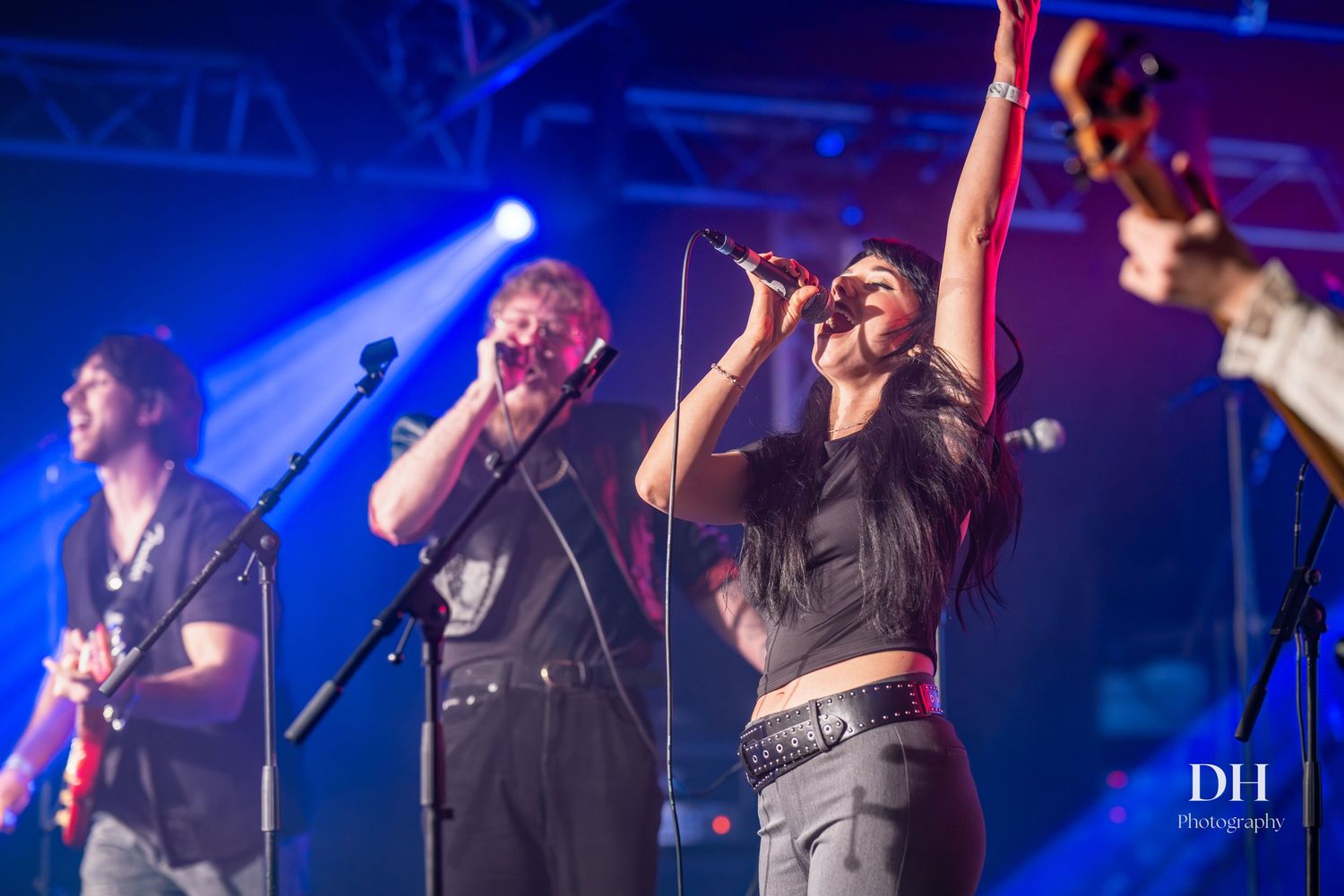 Three-piece band performing on stage under blue lights with singer raising arm at live show.
