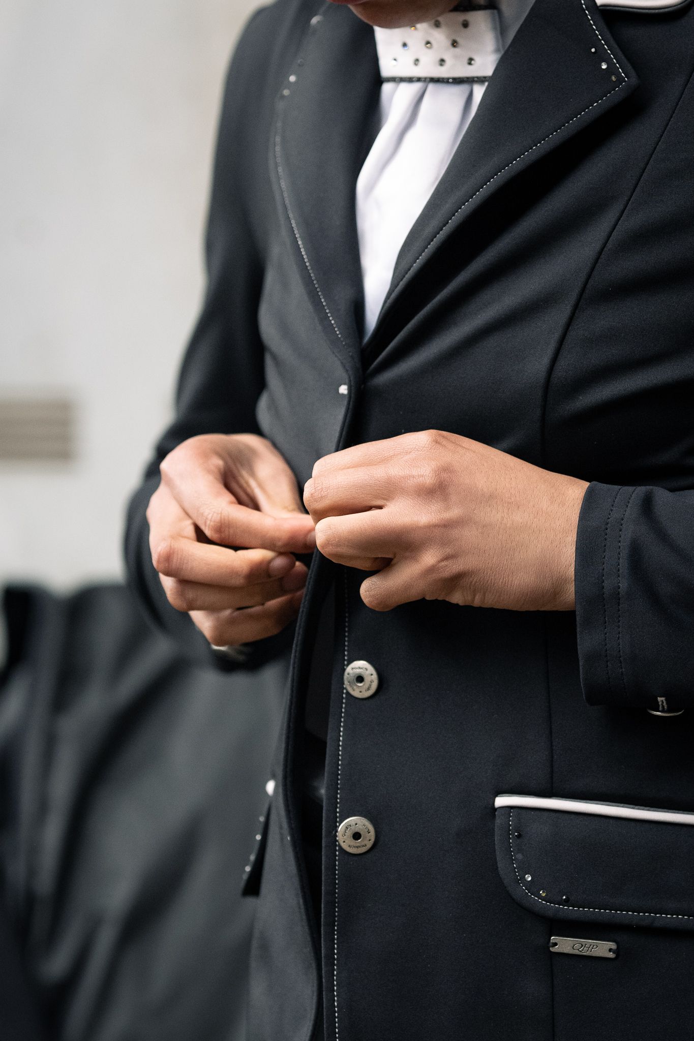 Equestrian buttoning a dark show jacket with white shirt and stock tie.