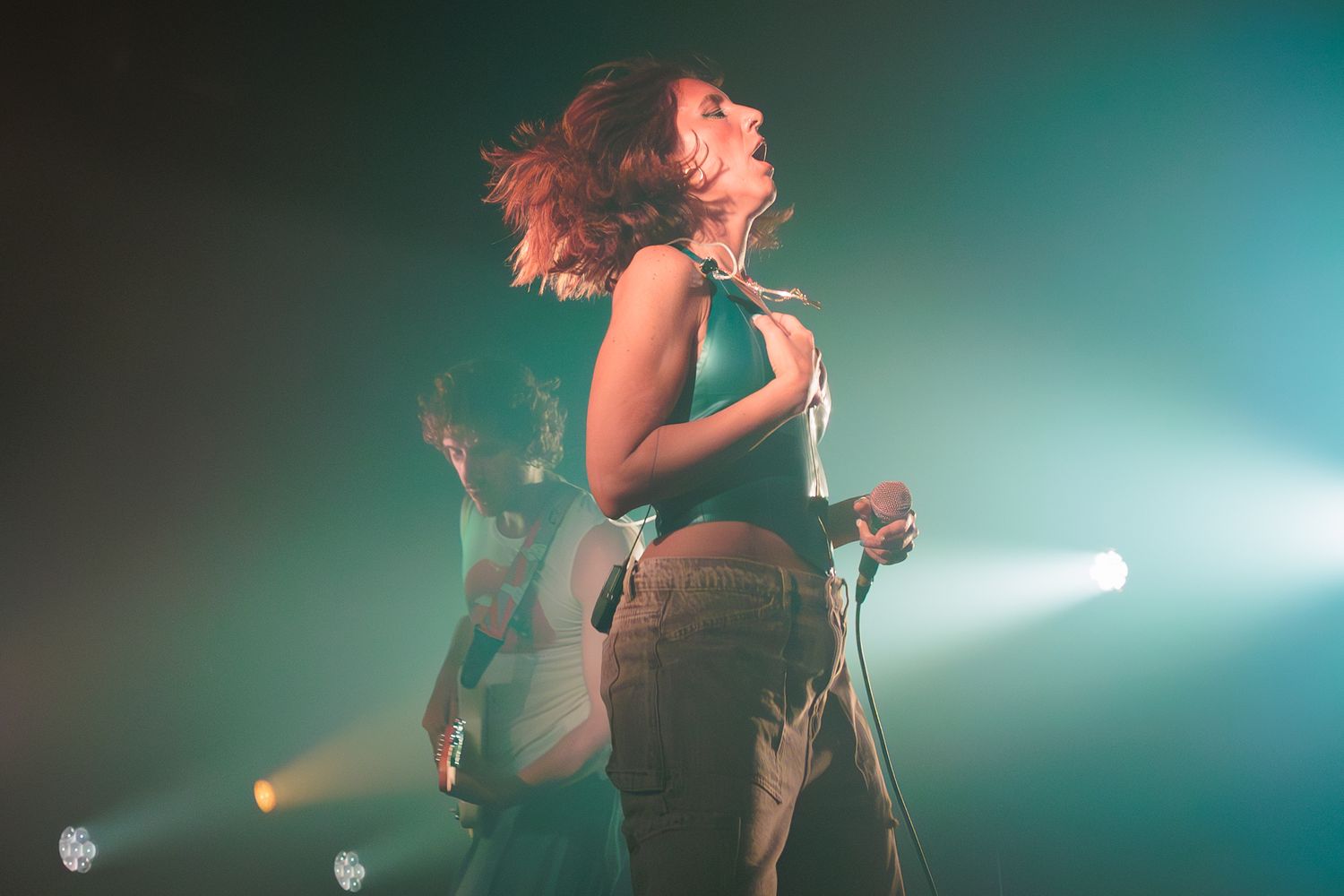 Female performer dancing energetically on stage under colorful spotlights during a live concert.