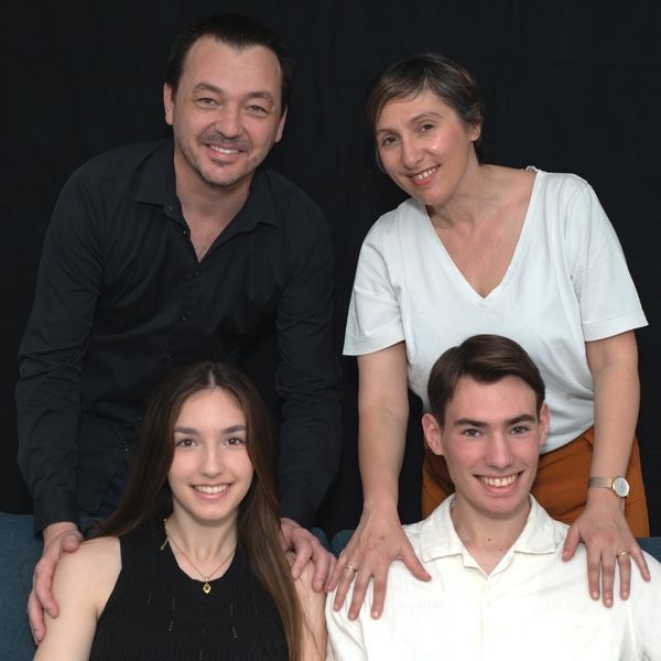 Family portrait of four people, two adults and two teens, smiling together.