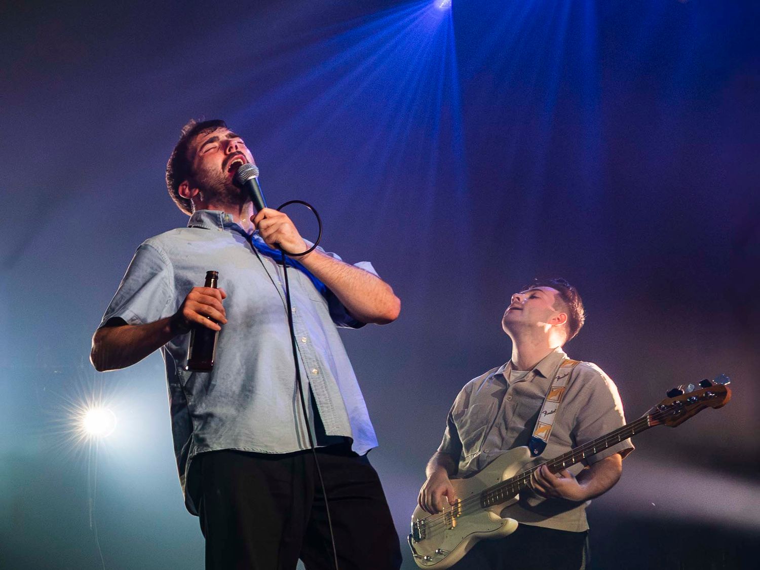 Singer performs with microphone while guitarist plays under blue stage lights at concert.