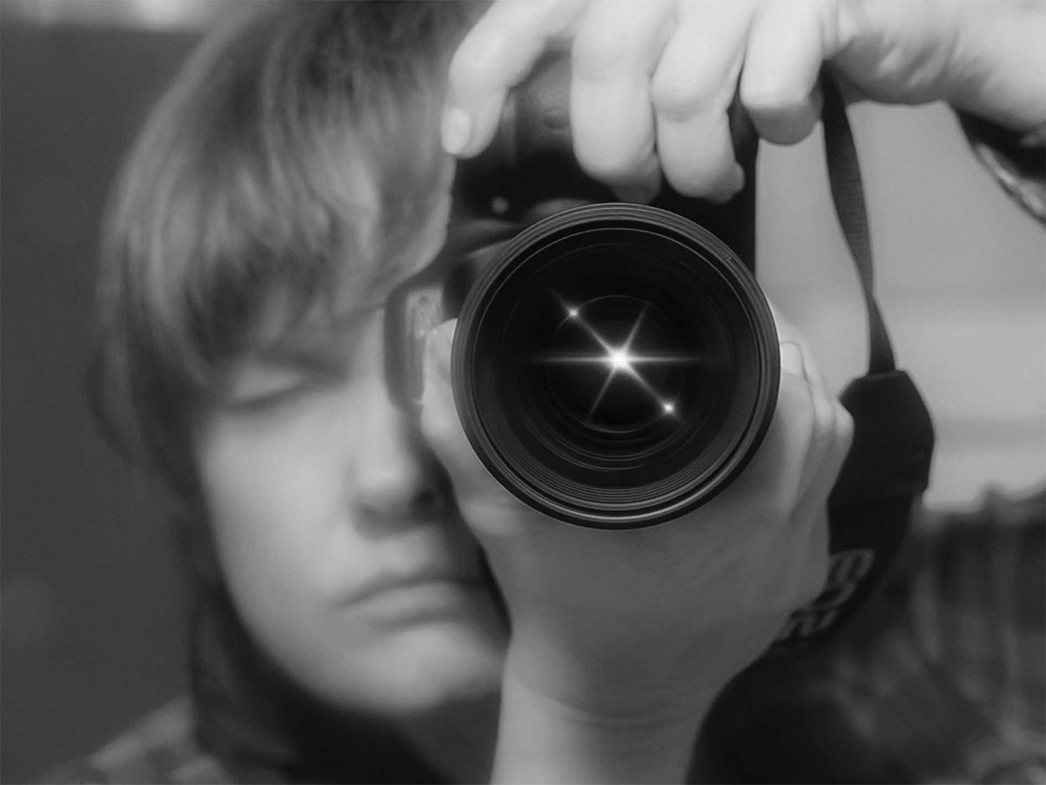 Black and white self-portrait of a photographer holding a DSLR camera with lens flare effect.