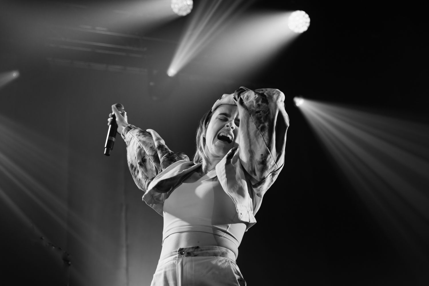 Black and white photo of a female performer singing passionately on stage under dramatic spotlights.