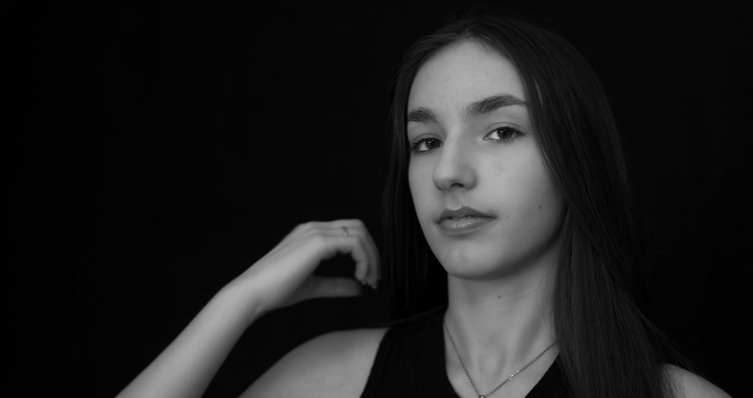Black and white portrait of a young woman with long dark hair against dark background.