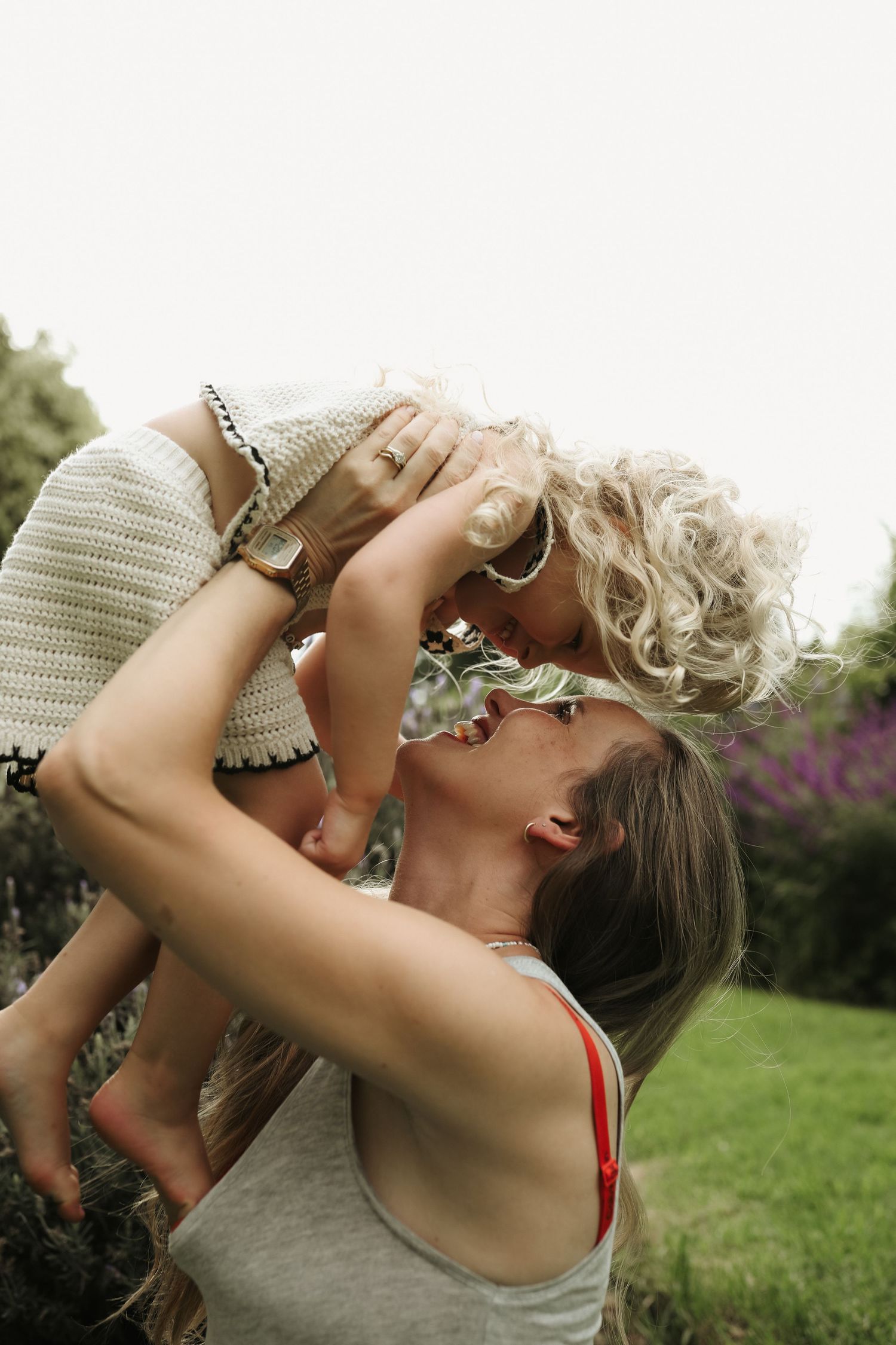 Mother lifting laughing daughter overhead in garden with wildflowers, Sydney family photographer