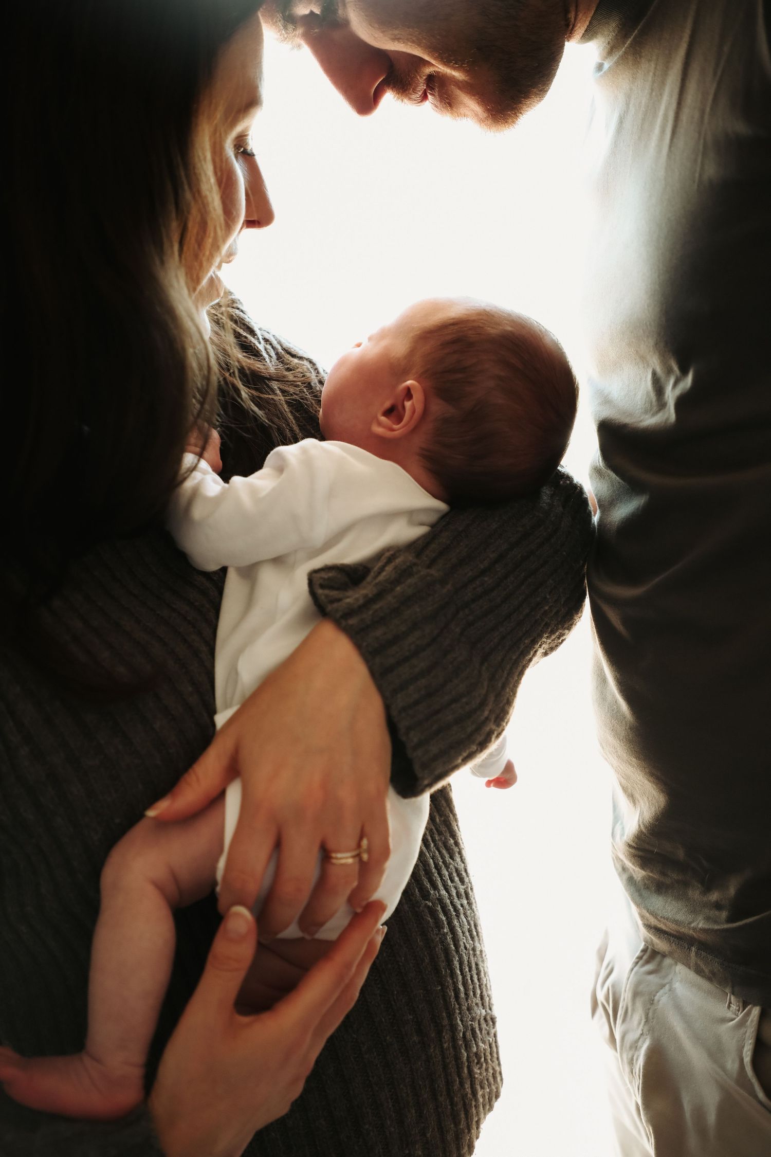 Parents cradling newborn baby in soft window light, in-home newborn photography Sydney
