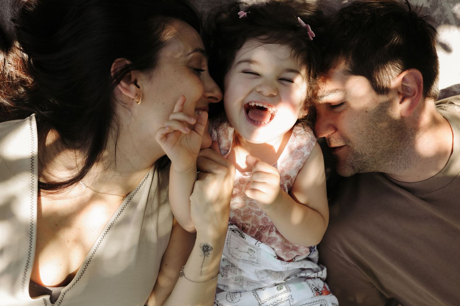 Parents laughing with toddler daughter in dappled sunlight, Sydney family photography