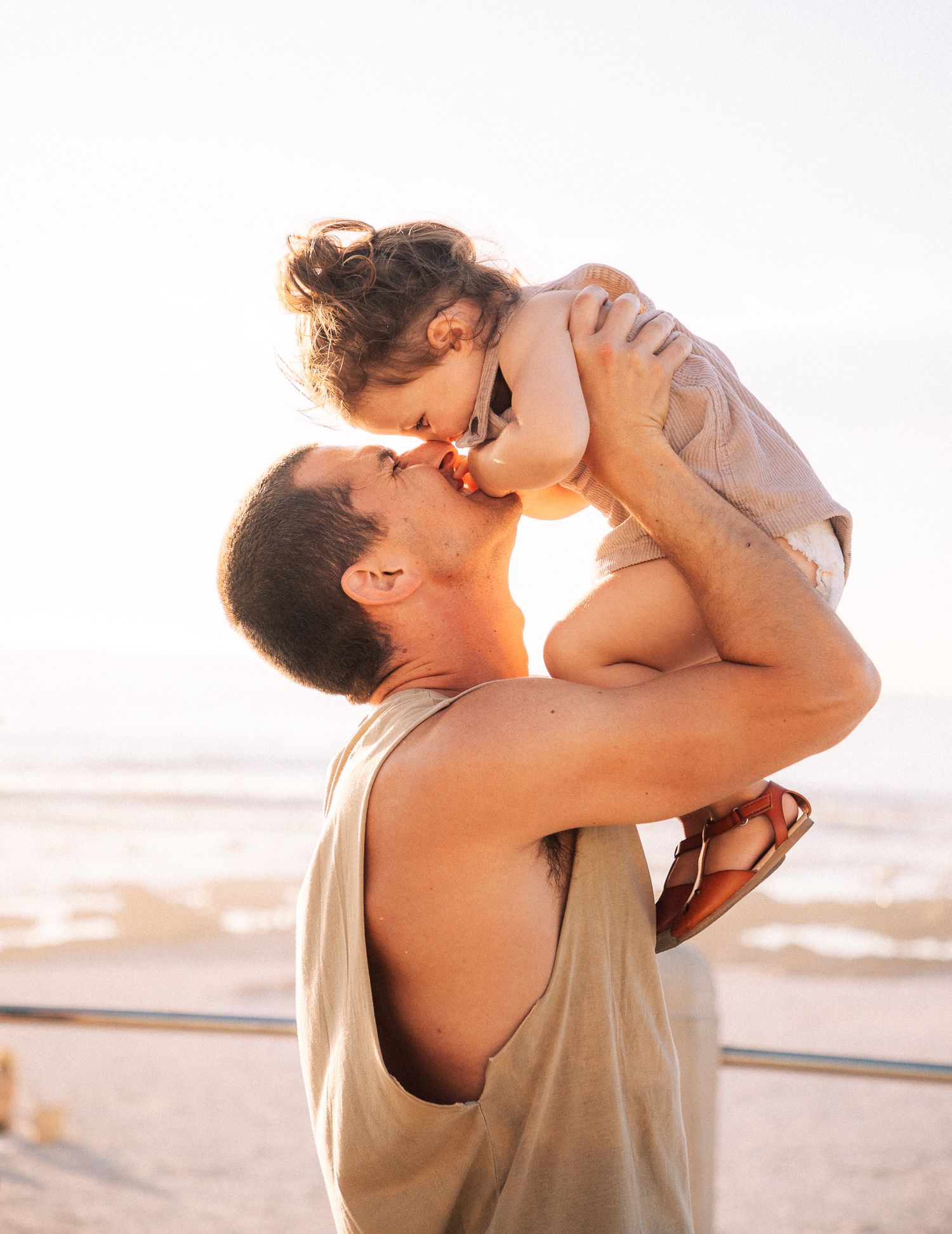 Father kissing toddler daughter while lifting her at sunset on the beach, Sydney family photography