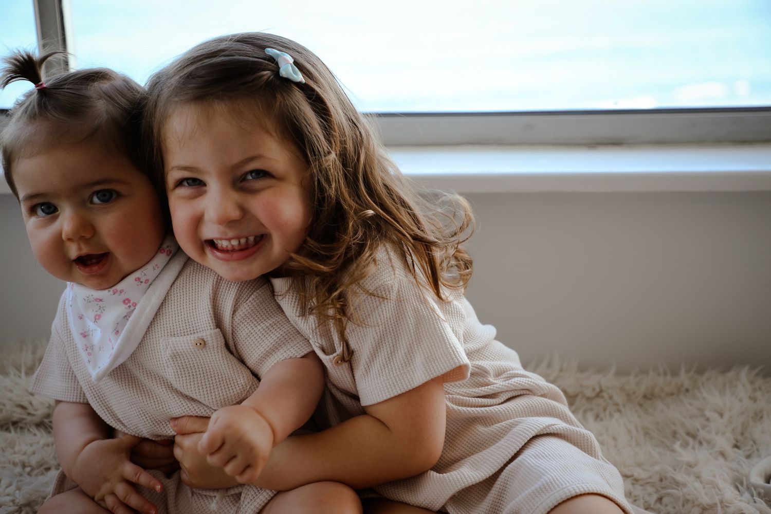 Two young sisters sitting together laughing by window, Sydney family photography