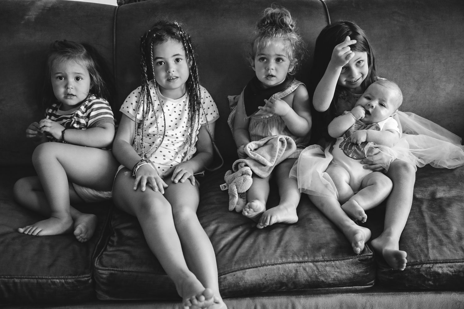 Black and white portrait of group of cousins sitting together on couch, in-home family photography Sydney