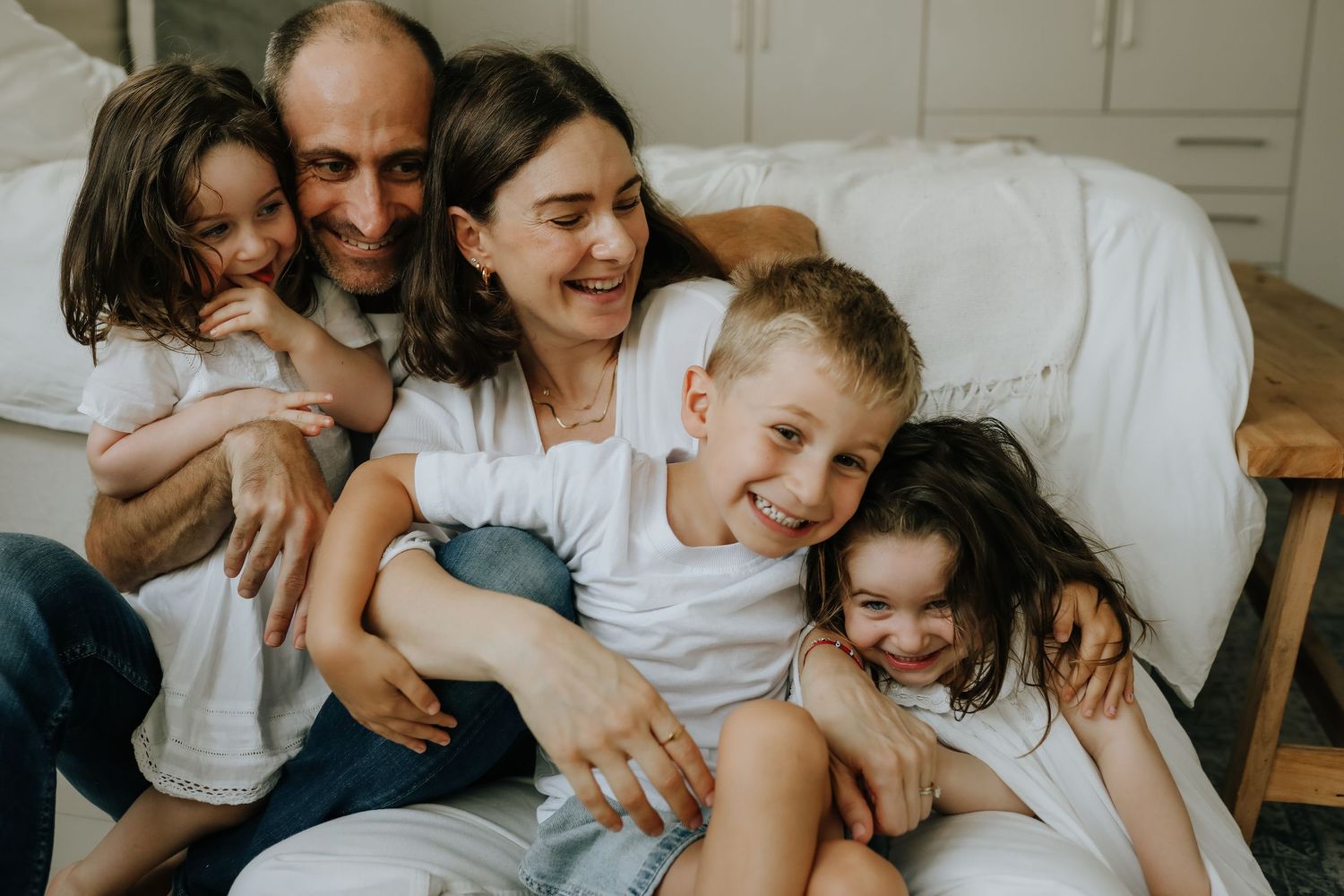Family of five laughing together in bedroom, in-home family photography Sydney