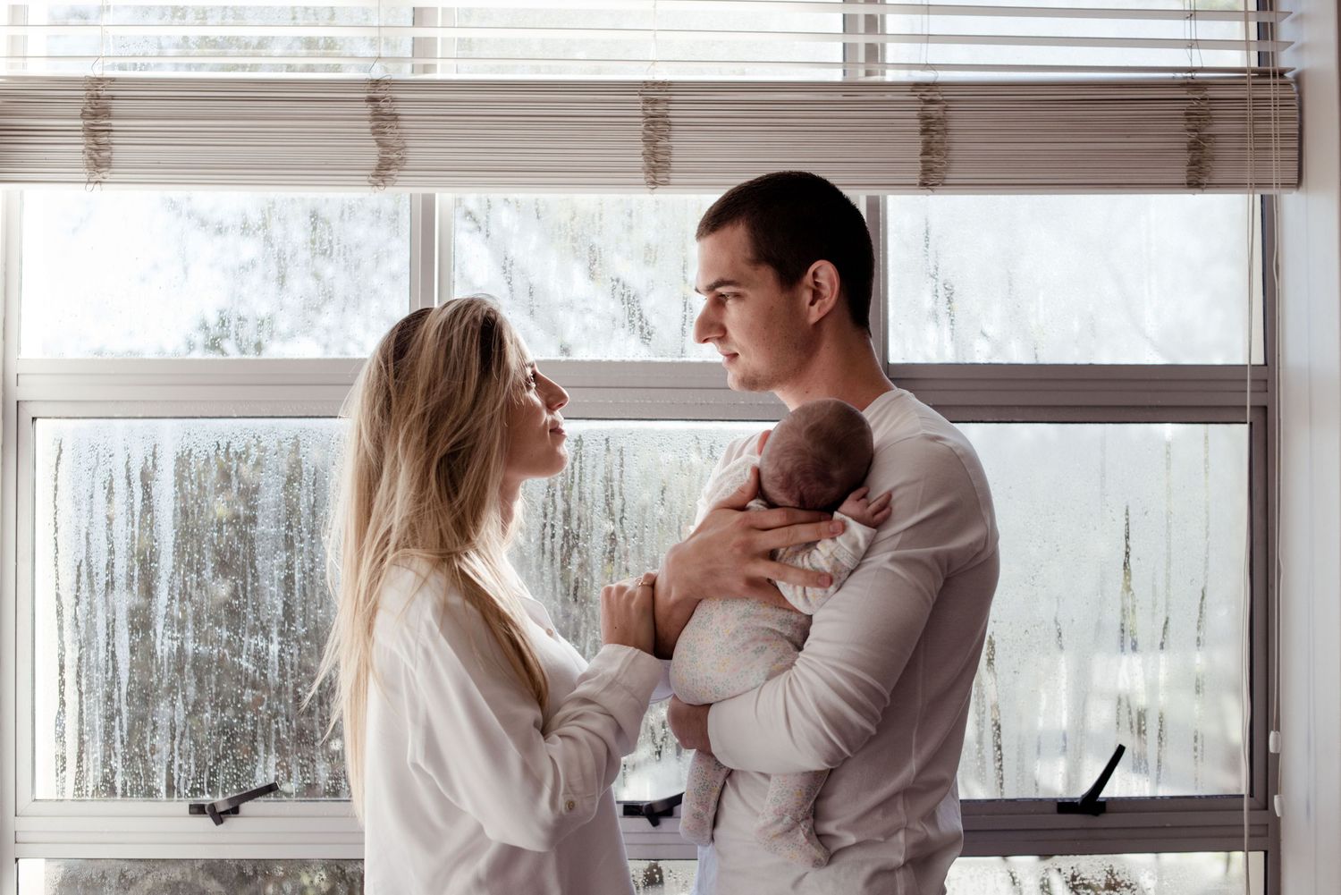 Parents holding newborn baby together by window, in-home newborn photography Sydney