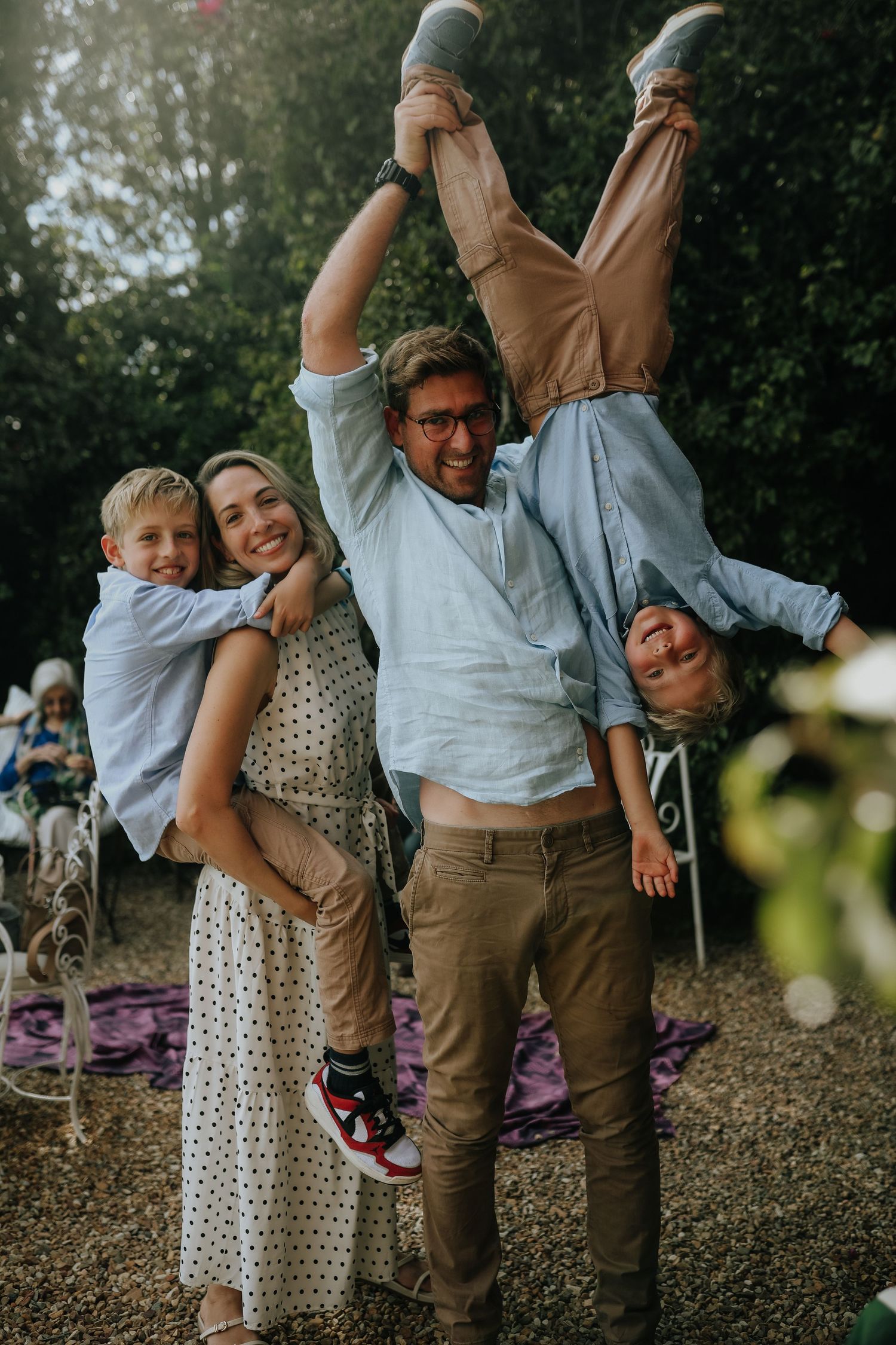 Dad playfully holding young son upside down while family laughs together in garden, Sydney family photography session